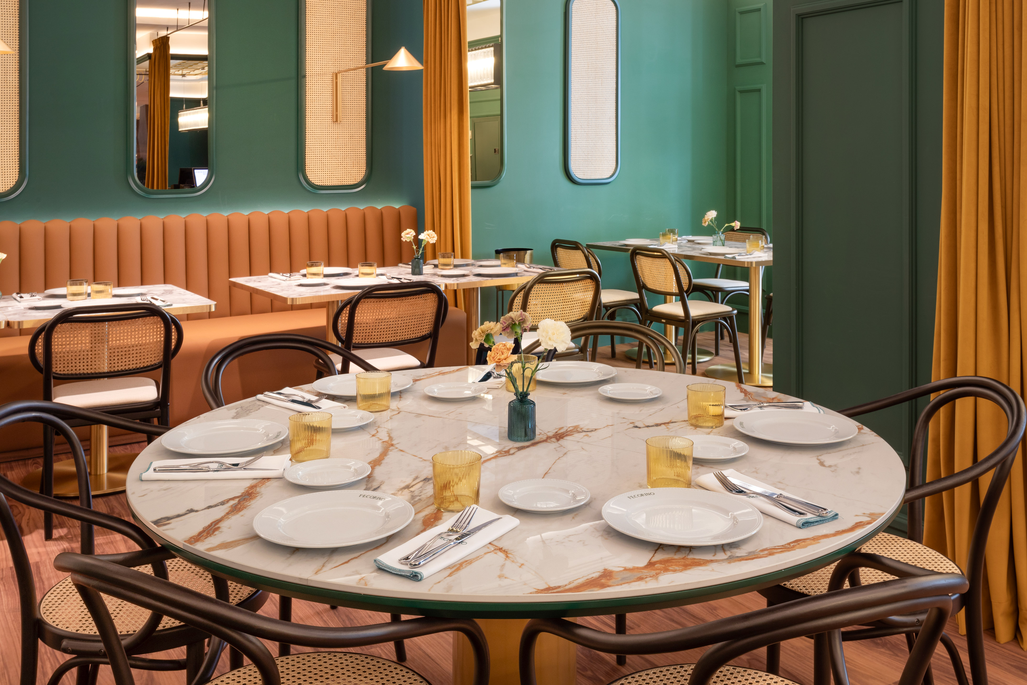 Restaurant dining room with green walls, marble tables, and dark cane chairs.