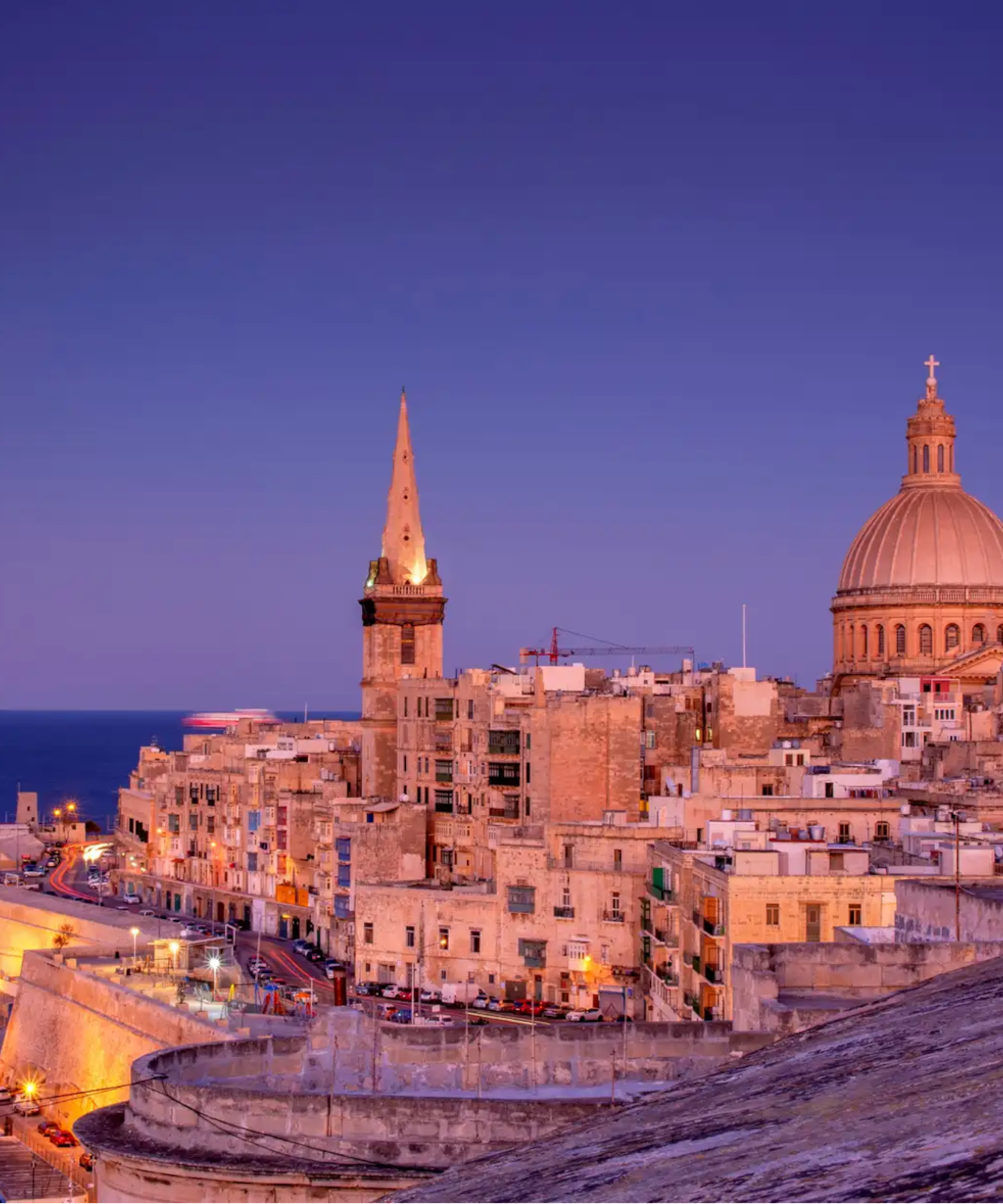 Valletta, Malta cityscape at dusk, dome, spire, historic buildings by the sea.