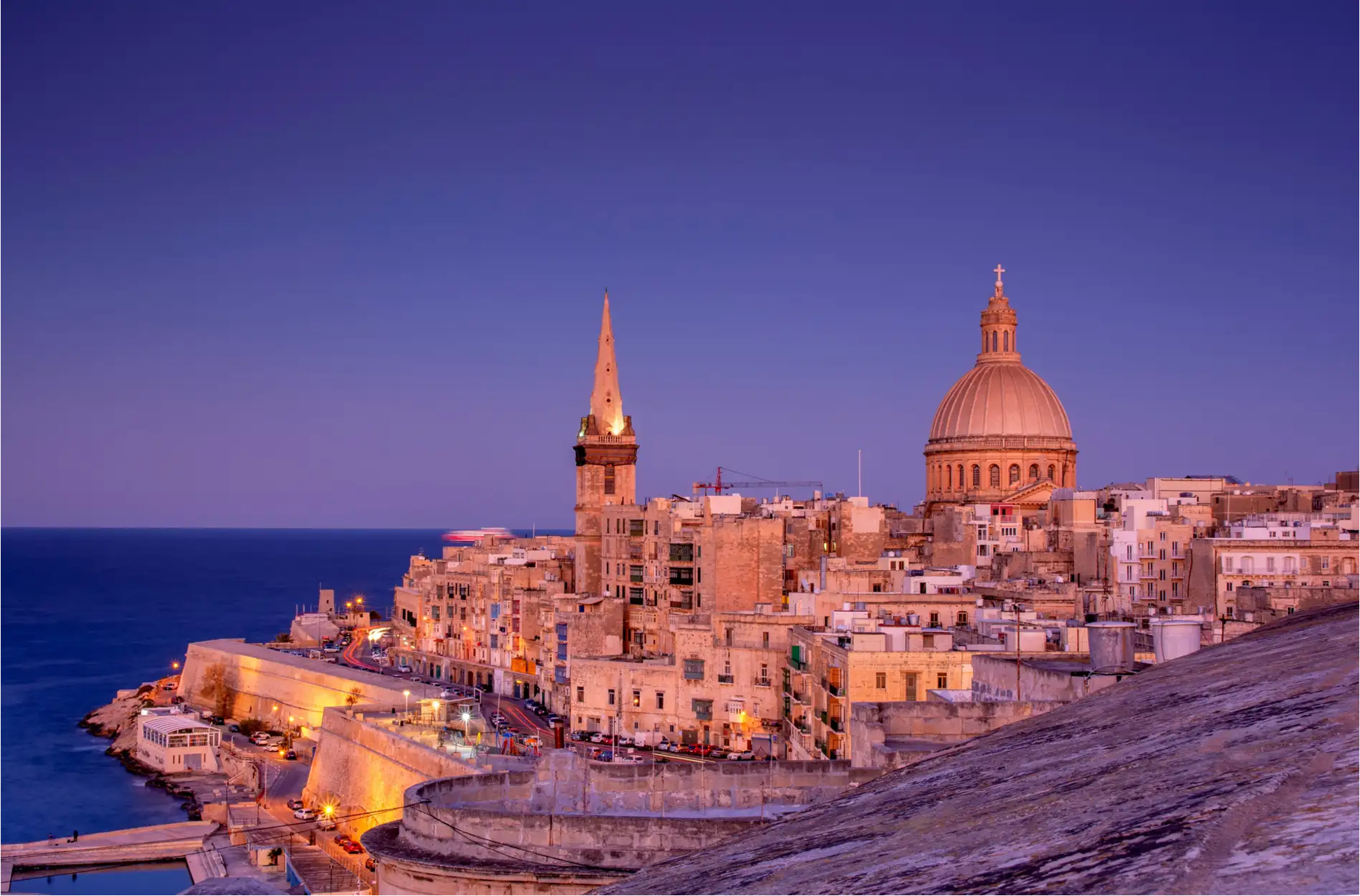 Valletta, Malta cityscape at dusk, dome, spire, historic buildings by the sea.