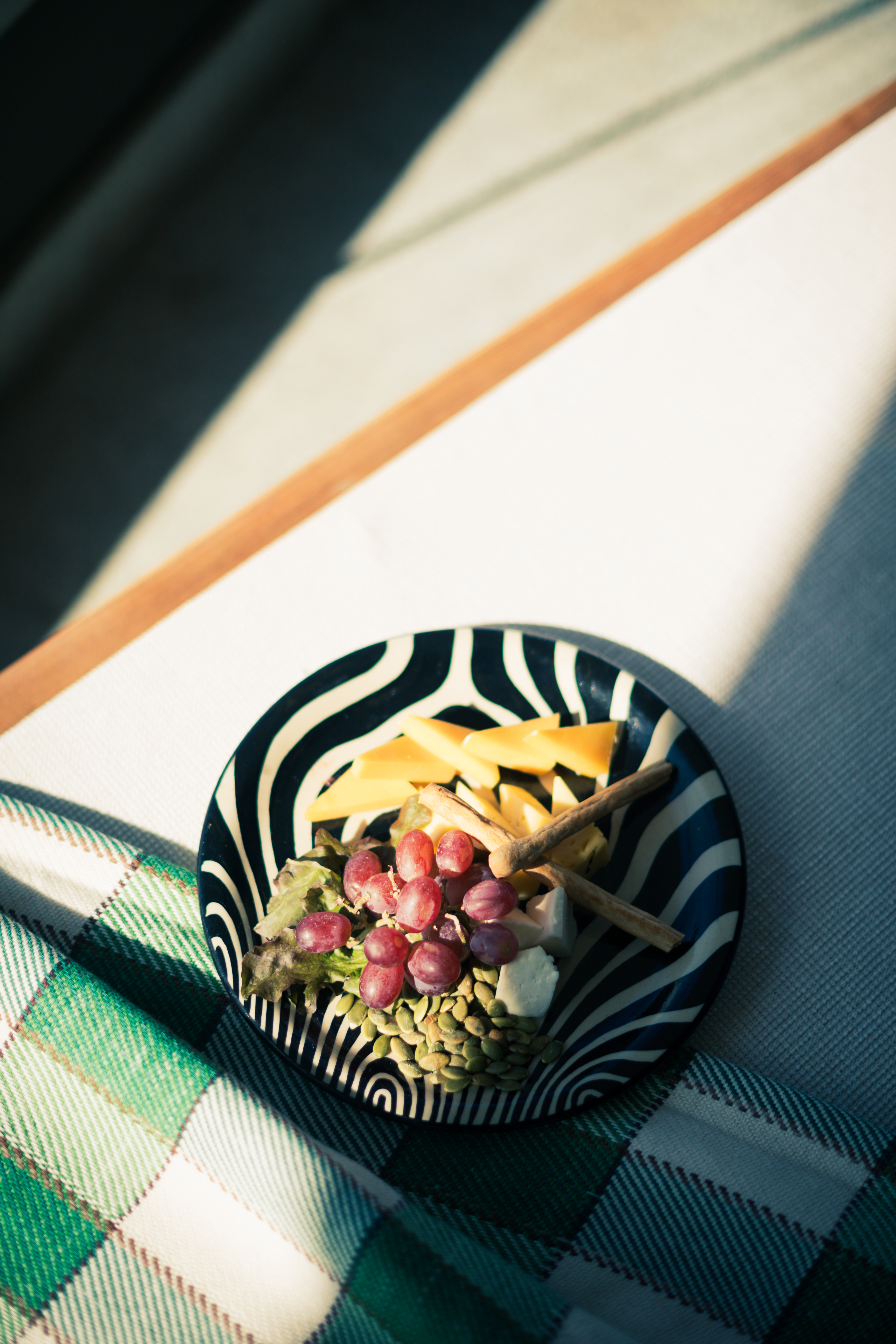 Zebra-patterned plate with grapes, cheeses, pumpkin seeds, breadsticks on plaid.