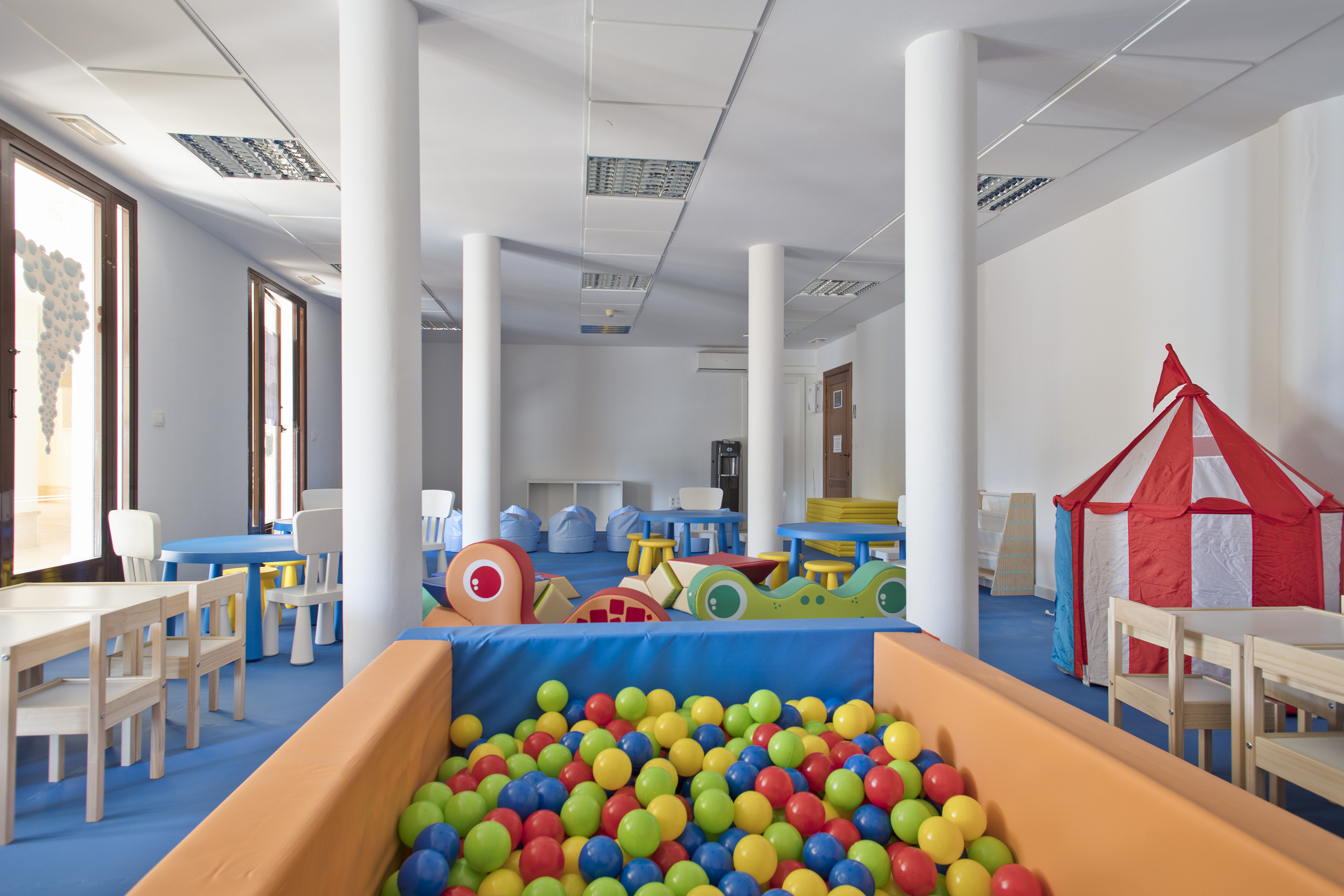 Colorful indoor kids' club with ball pit, small furniture, and play tent.