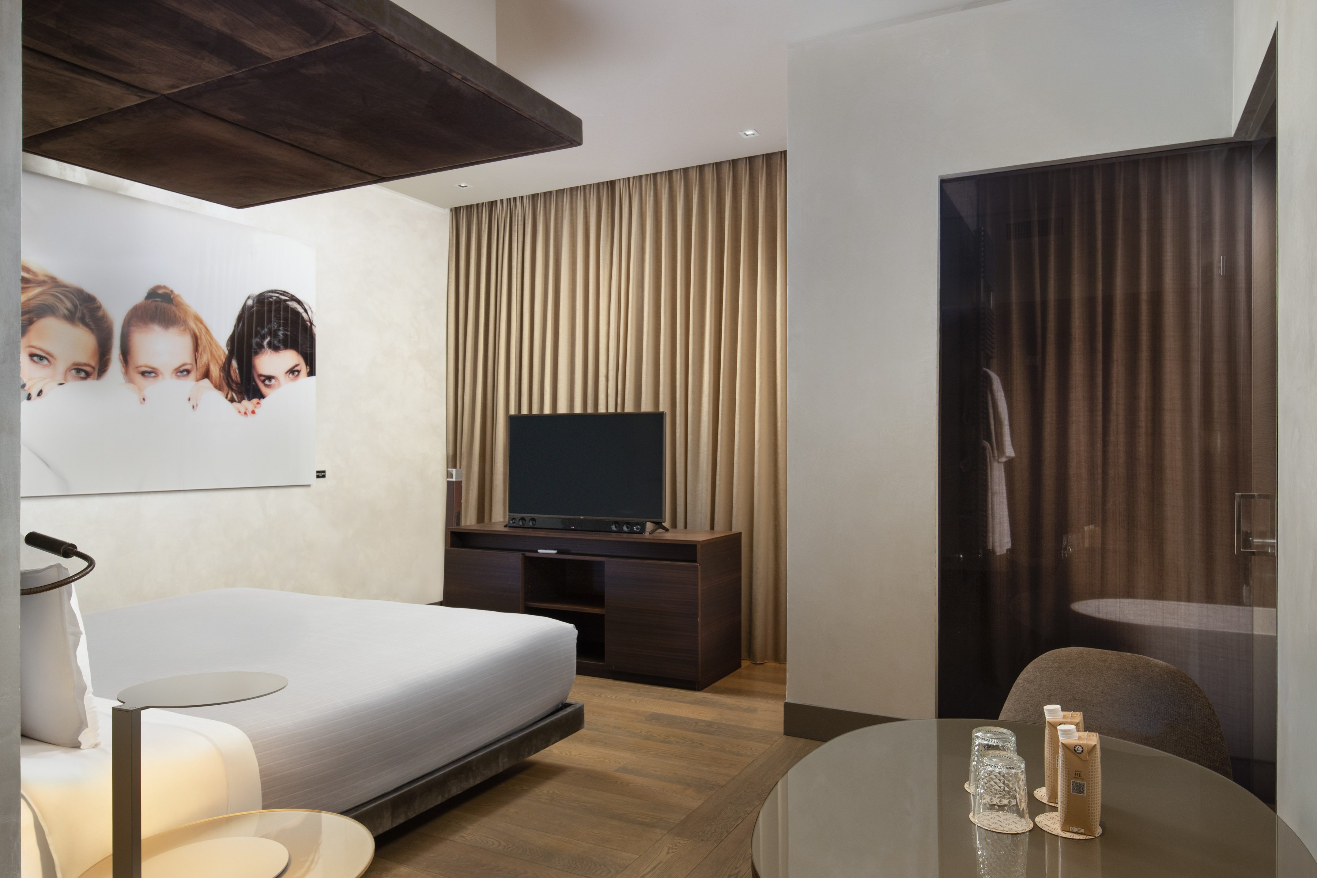 Sleek hotel room: bed, TV, dark wood accents, bold women's portrait artwork.