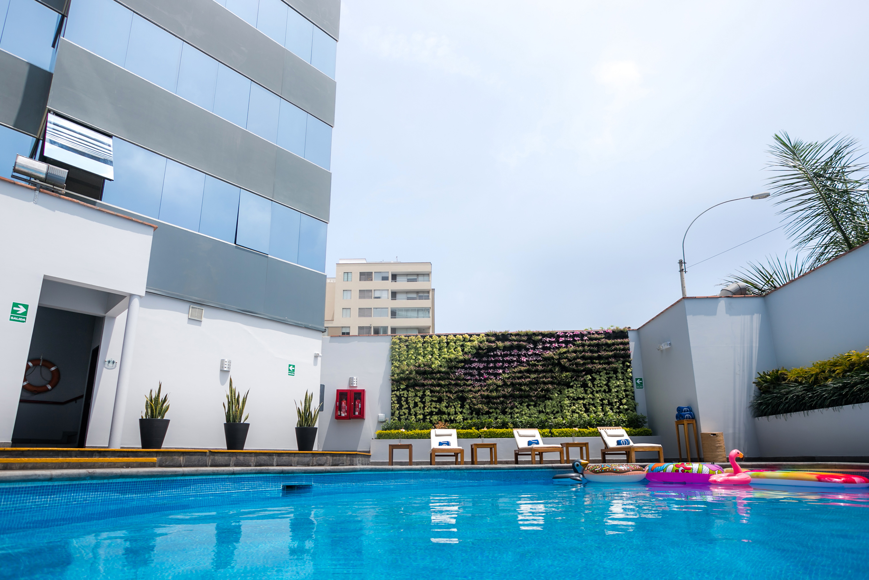 Hotel swimming pool with vertical garden, lounge chairs, and colorful floats.