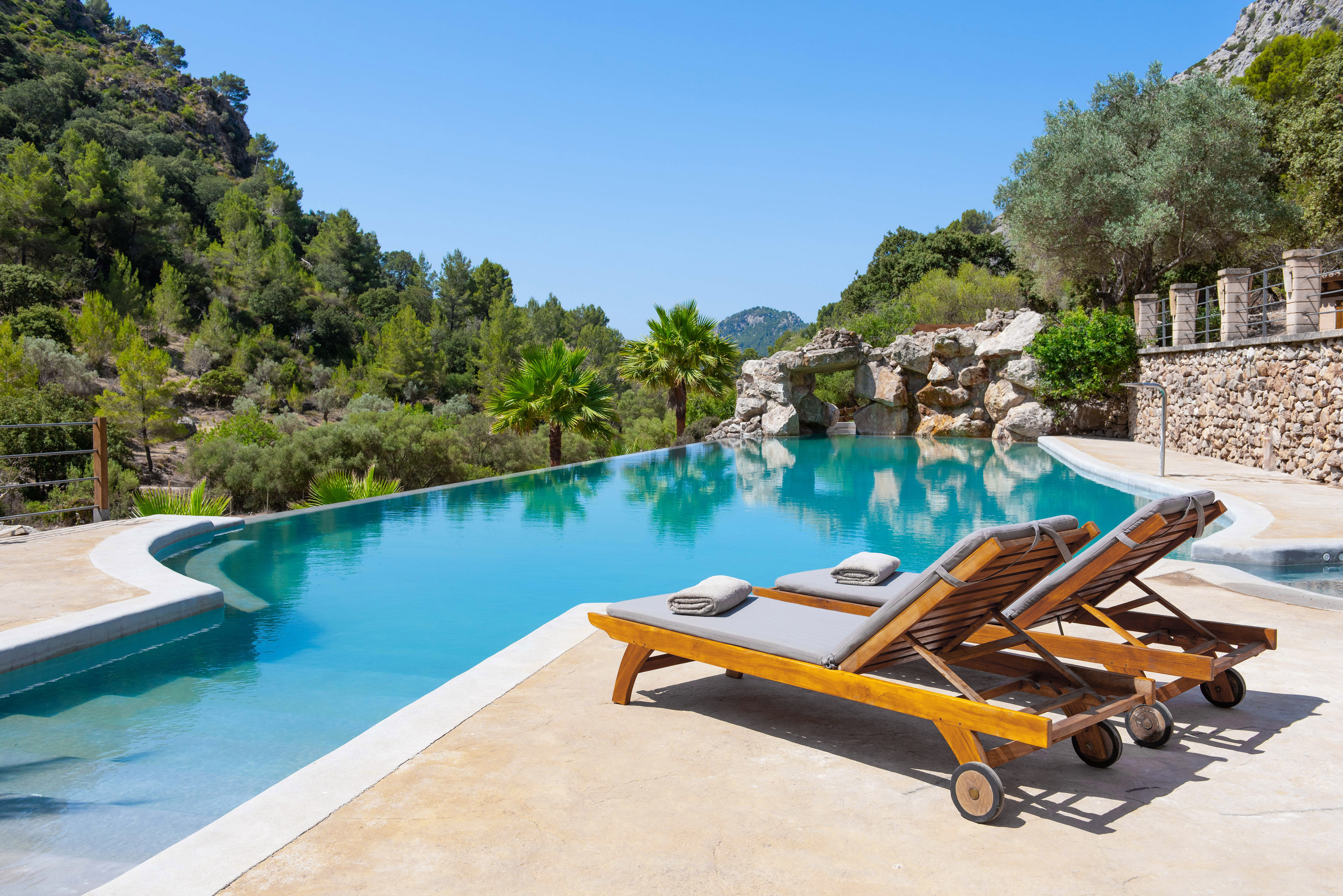 Infinity pool, sun loungers, and lush green mountains under a clear sky.
