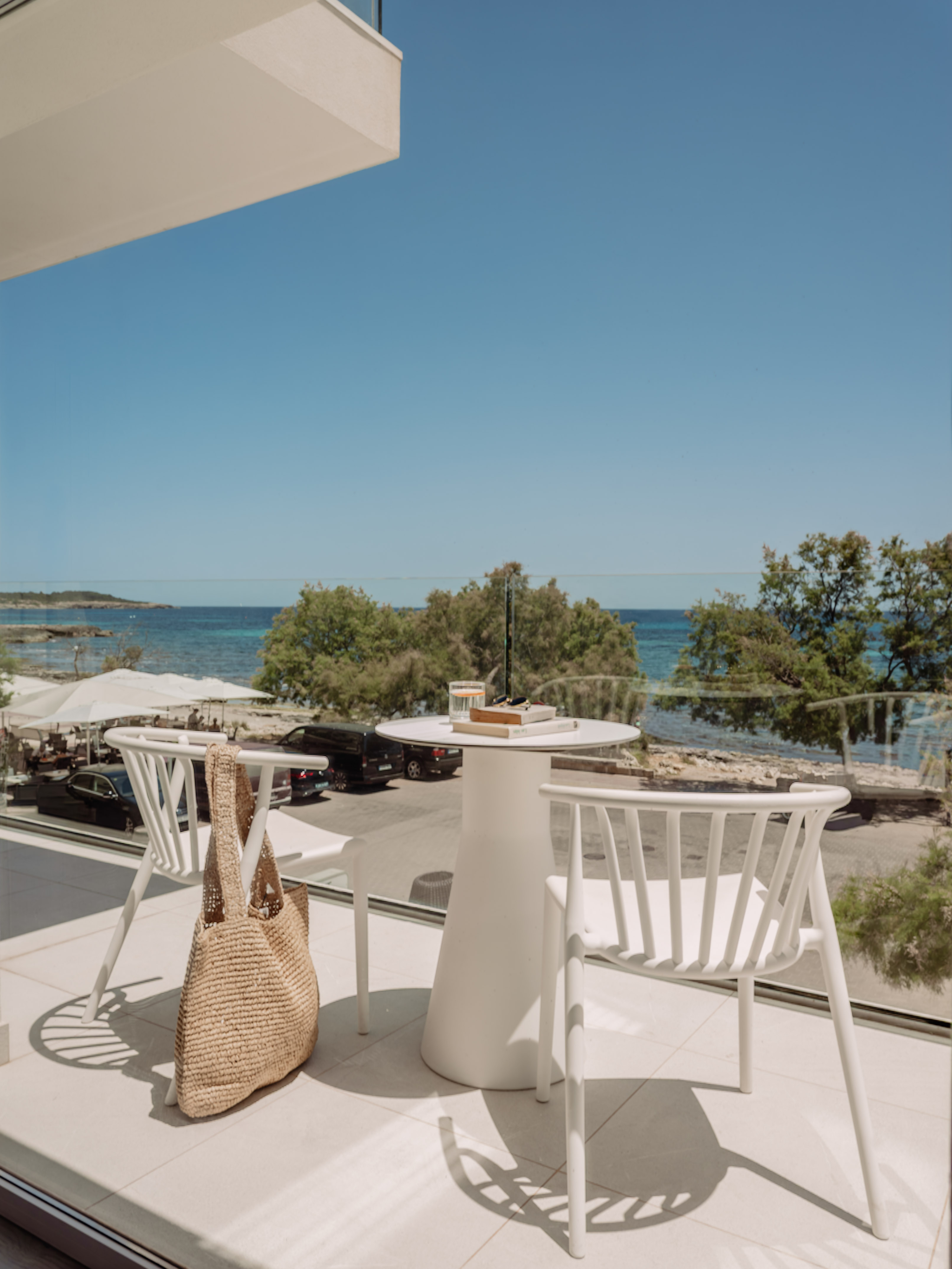 Balcón de hotel con mesa y sillas blancas, vistas al mar Mediterráneo.