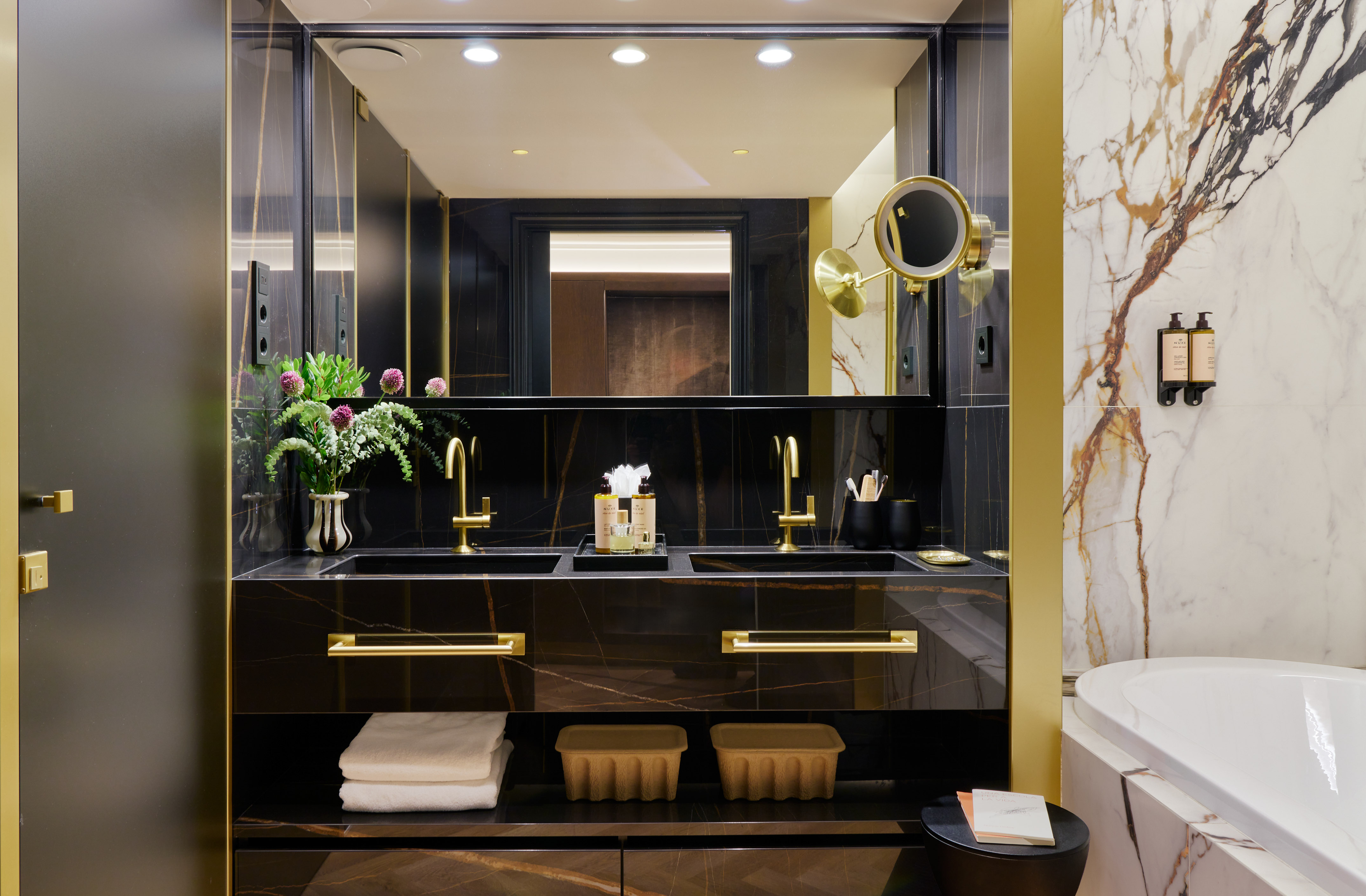 Luxury bathroom with black marble double vanity, gold fixtures, and white marble wall.