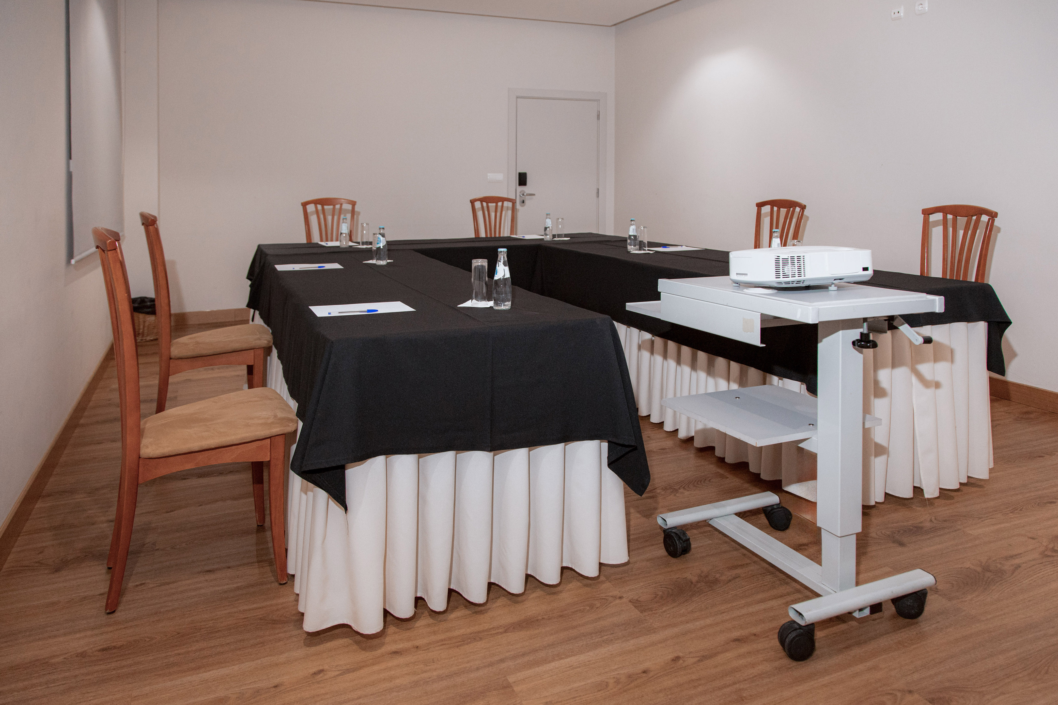 U-shaped meeting room with black tables, wooden chairs, and projector setup.