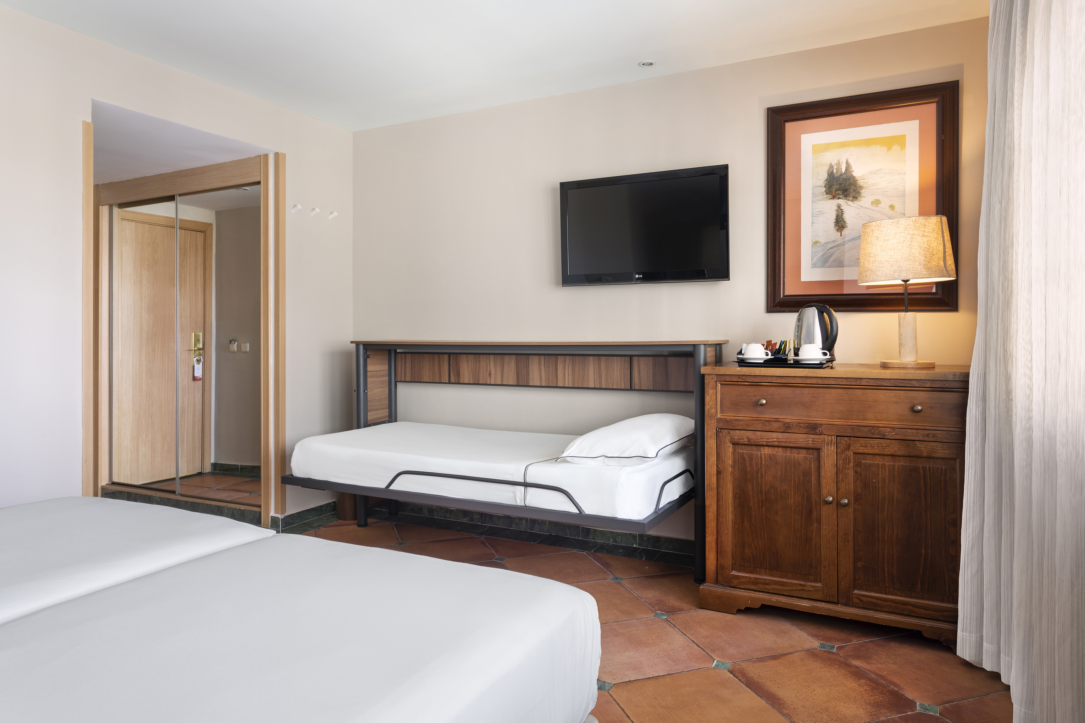 Hotel family room with twin beds, pull-out bed, TV, wooden cabinet, and tiled floor.