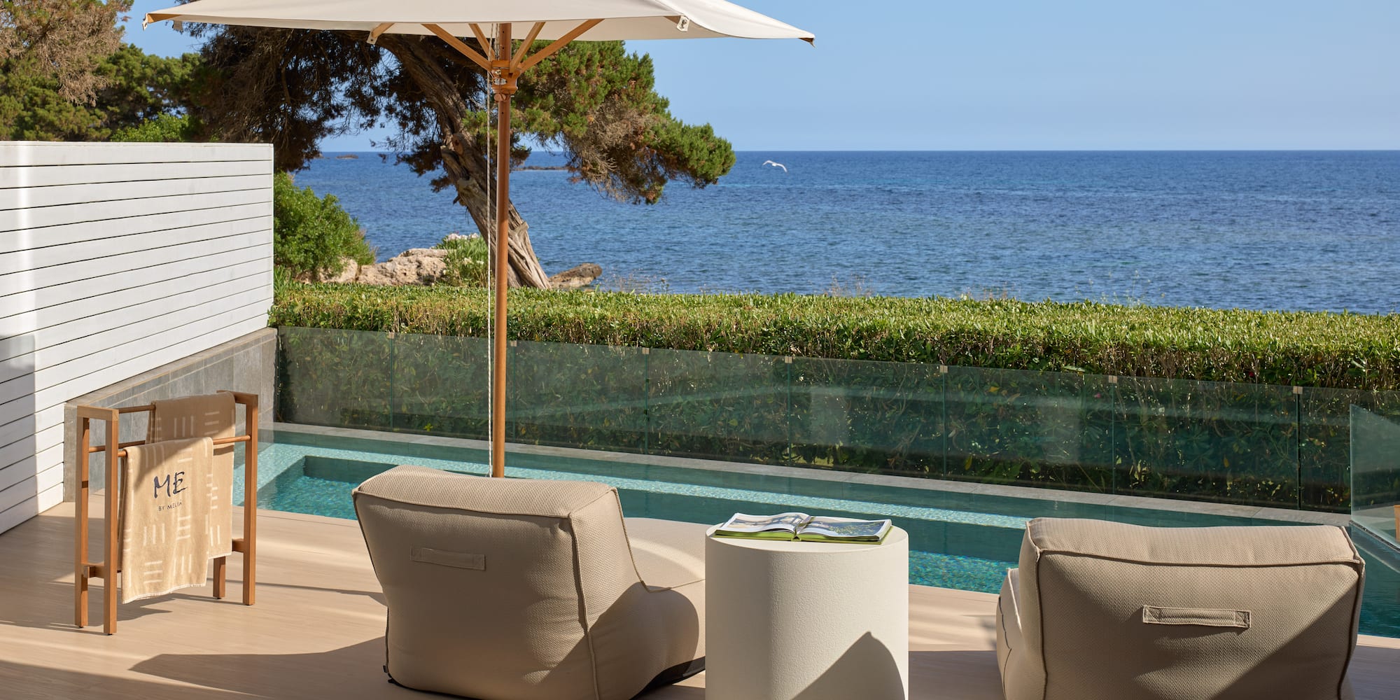 Resort patio with sea view, private pool, beige outdoor seating, and umbrella.