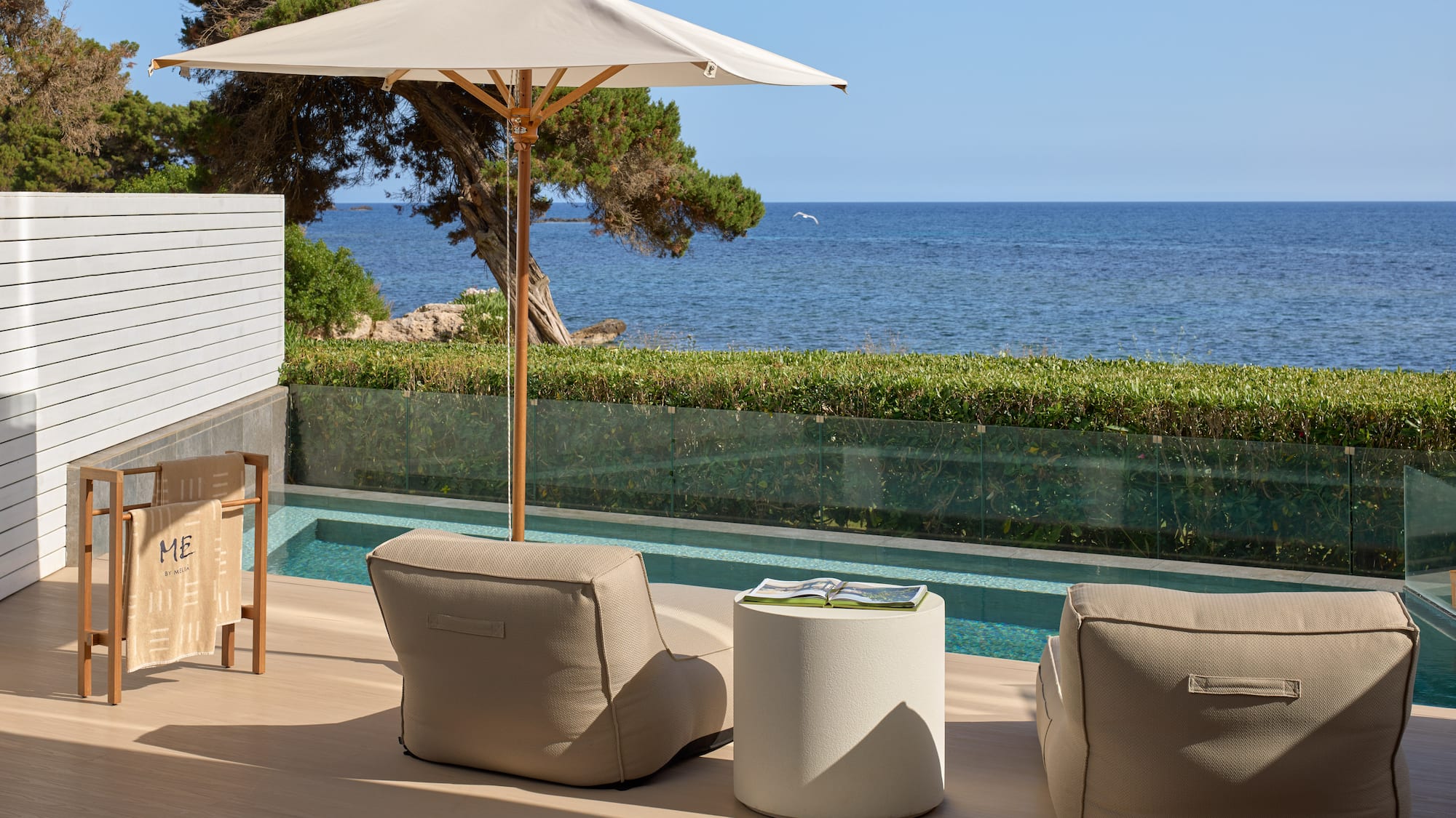 Resort patio with sea view, private pool, beige outdoor seating, and umbrella.