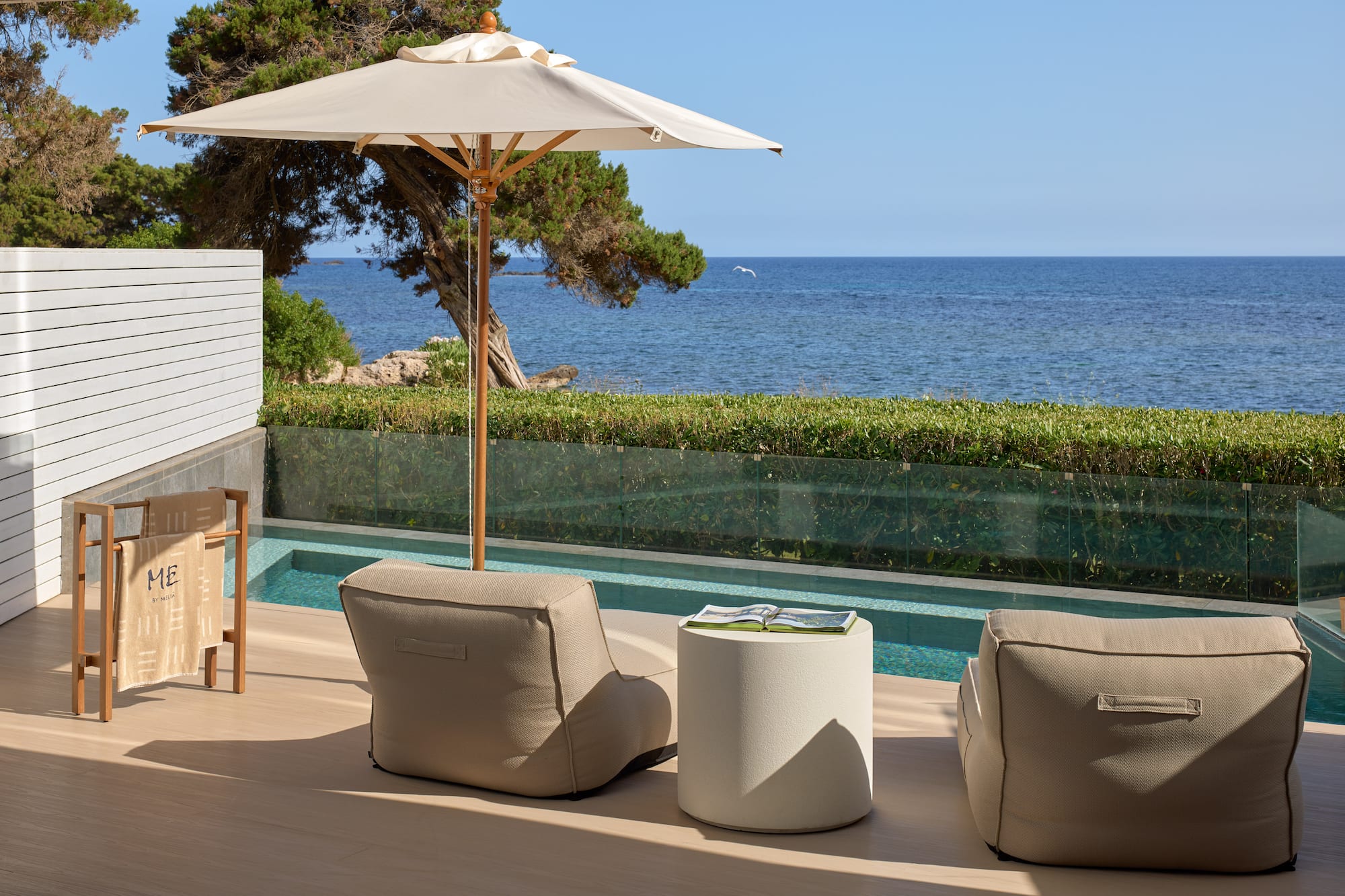 Resort patio with sea view, private pool, beige outdoor seating, and umbrella.