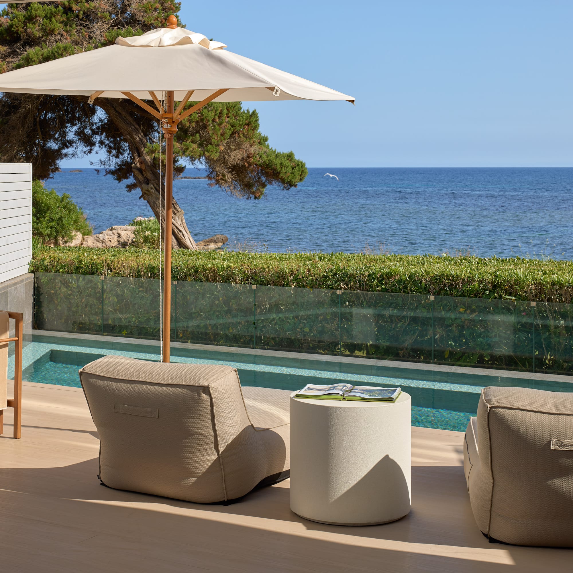 Resort patio with sea view, private pool, beige outdoor seating, and umbrella.