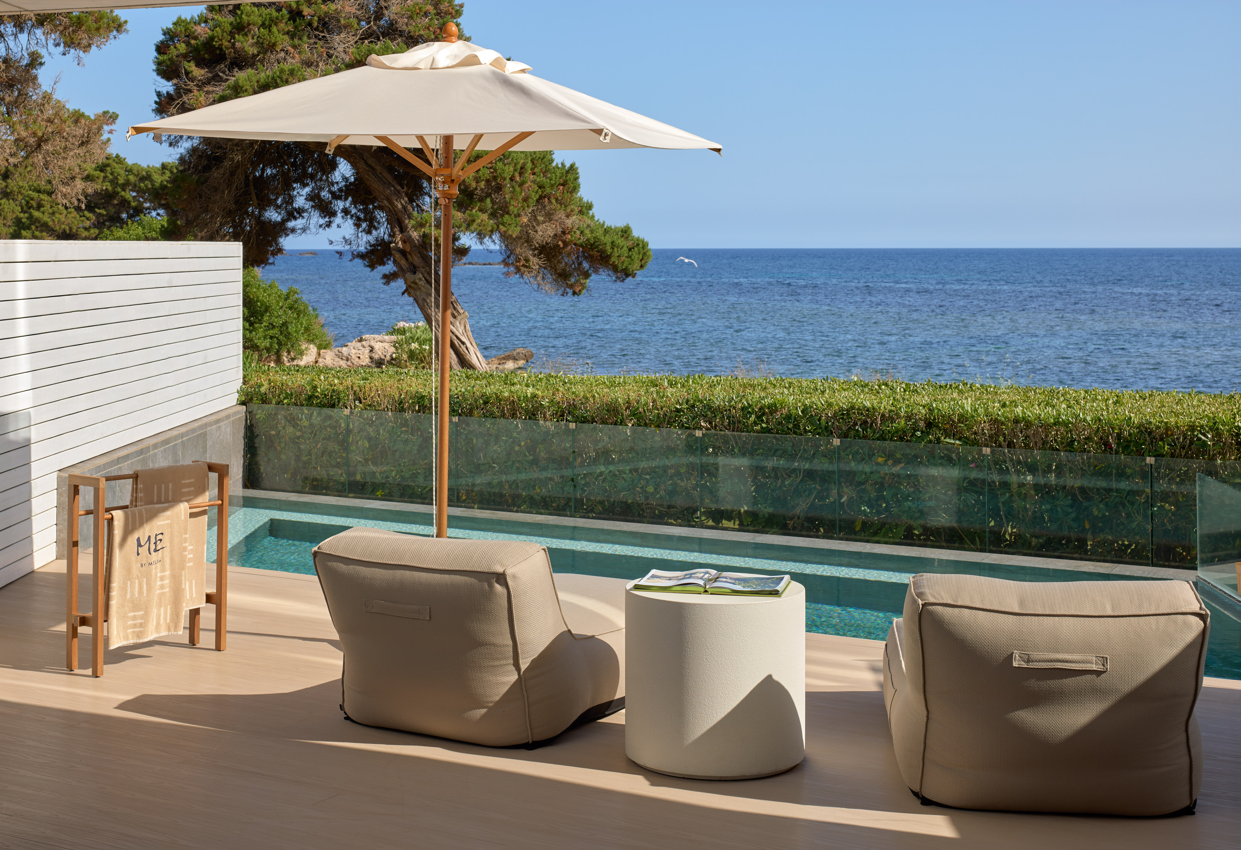 Resort patio with sea view, private pool, beige outdoor seating, and umbrella.