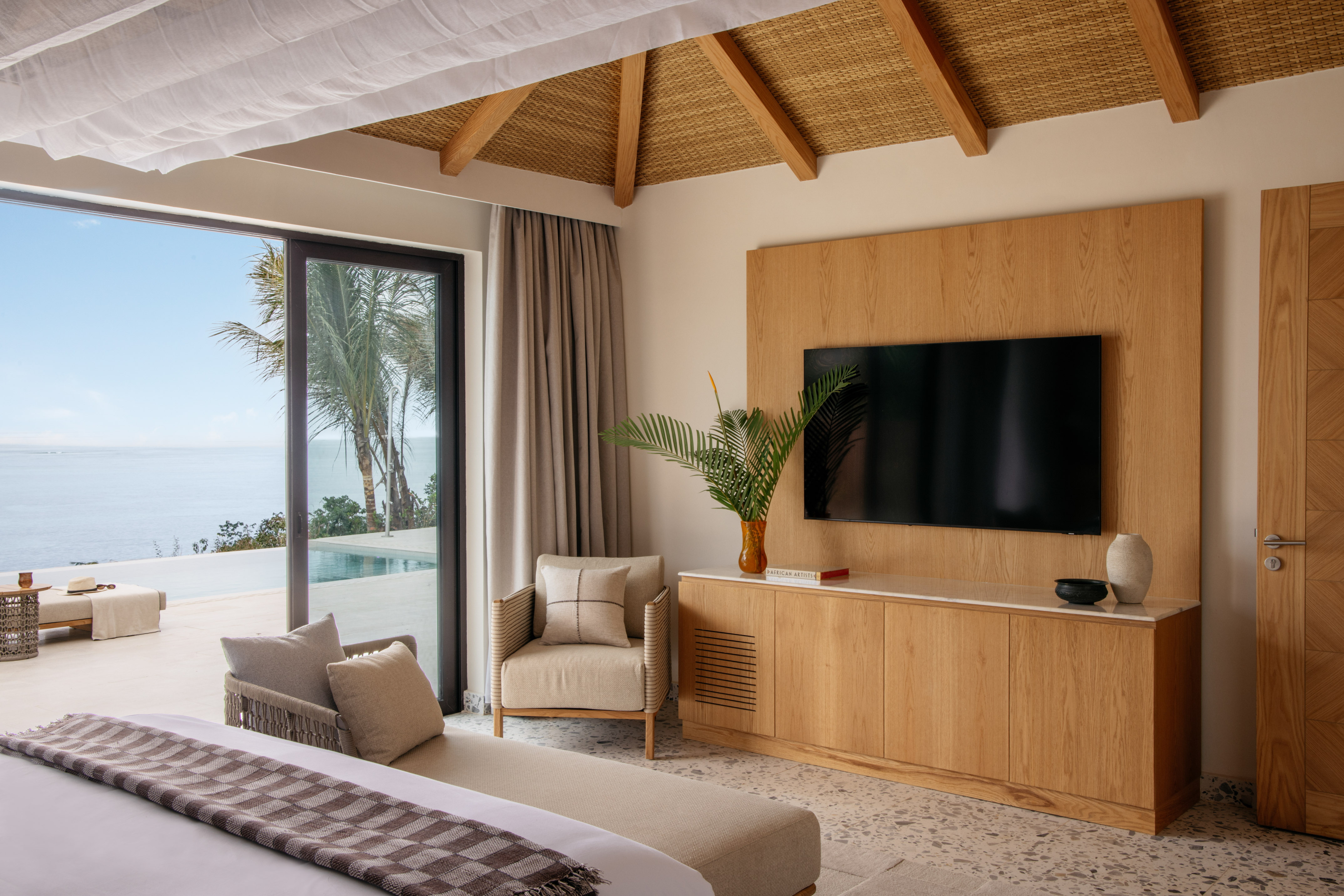 Modern tropical bedroom with ocean view, wooden TV unit, and resort design.