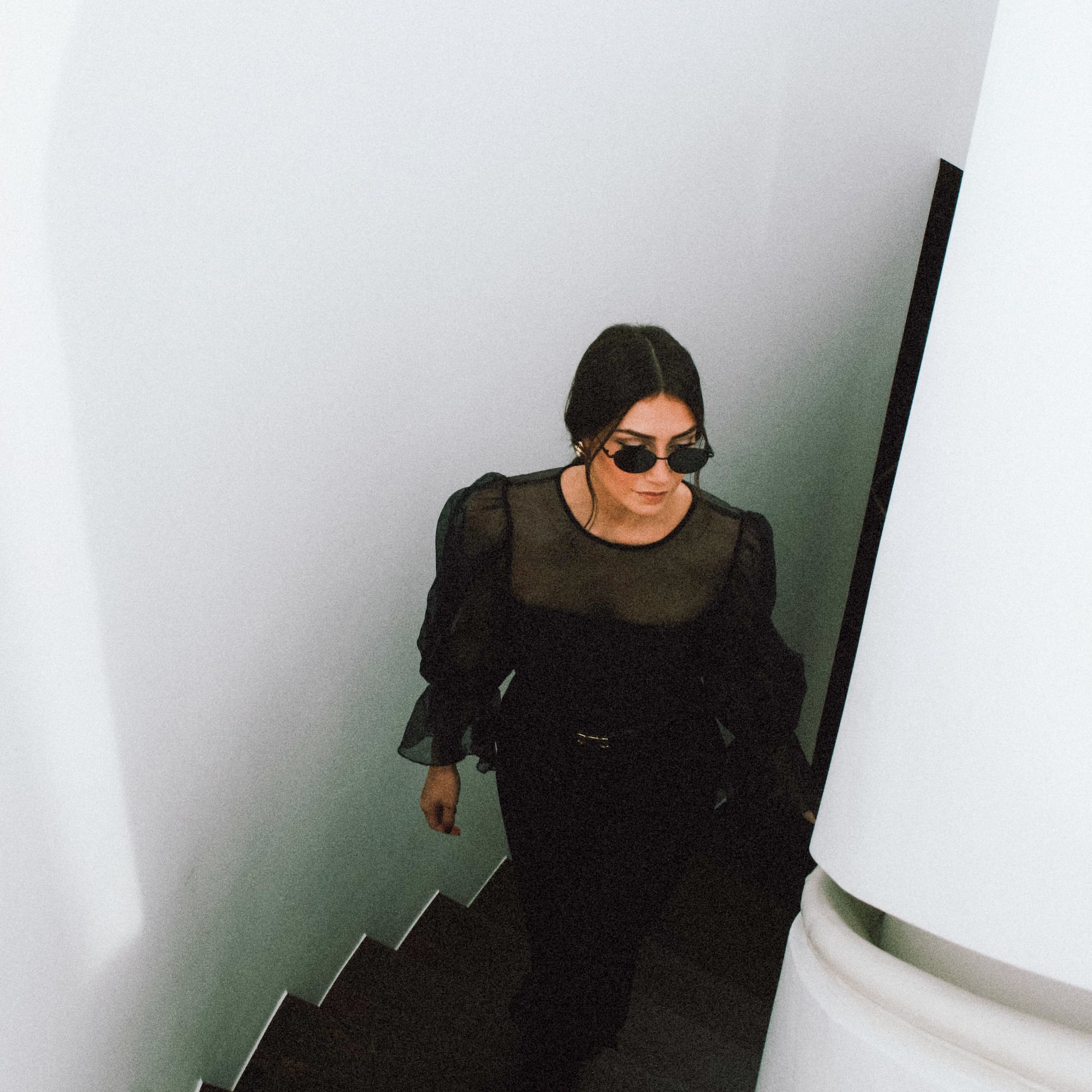 a woman in a black dress and sunglasses walking up stairs