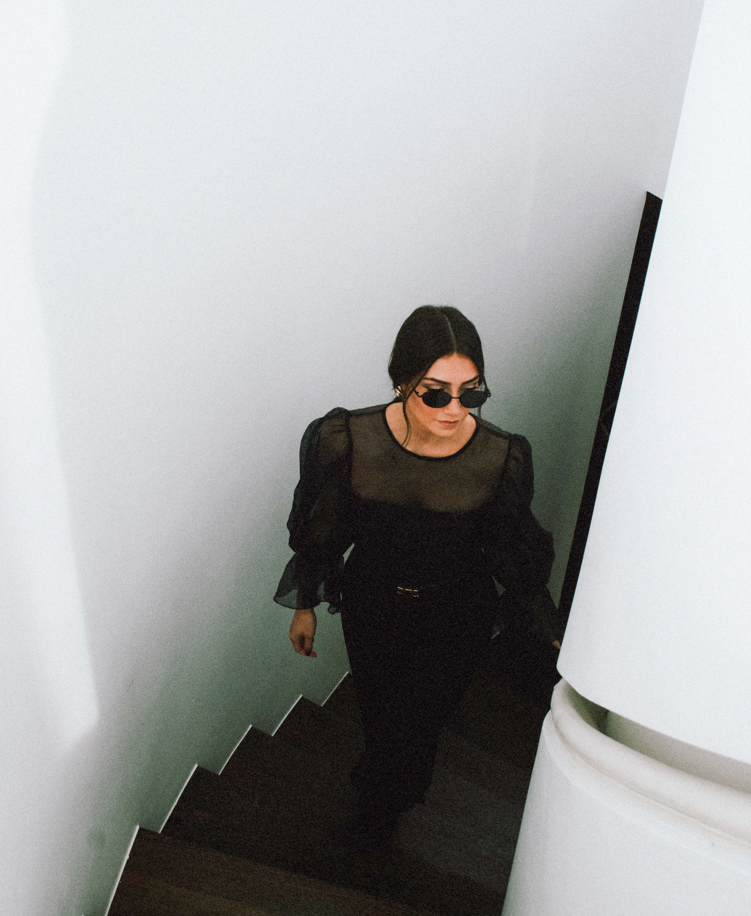 a woman in a black dress and sunglasses walking up stairs