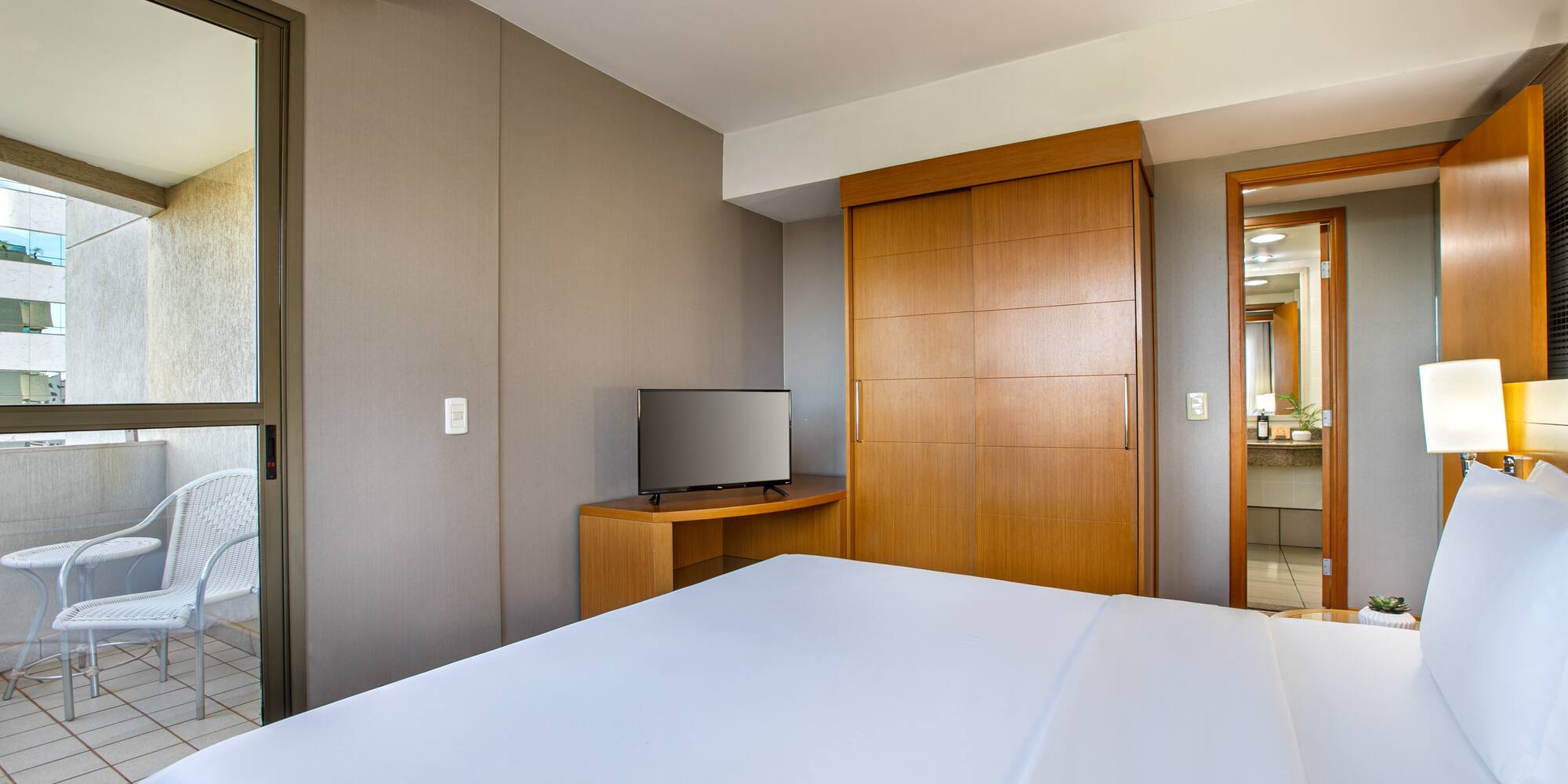 Clean hotel room with large white bed, TV, wooden wardrobe, and balcony.