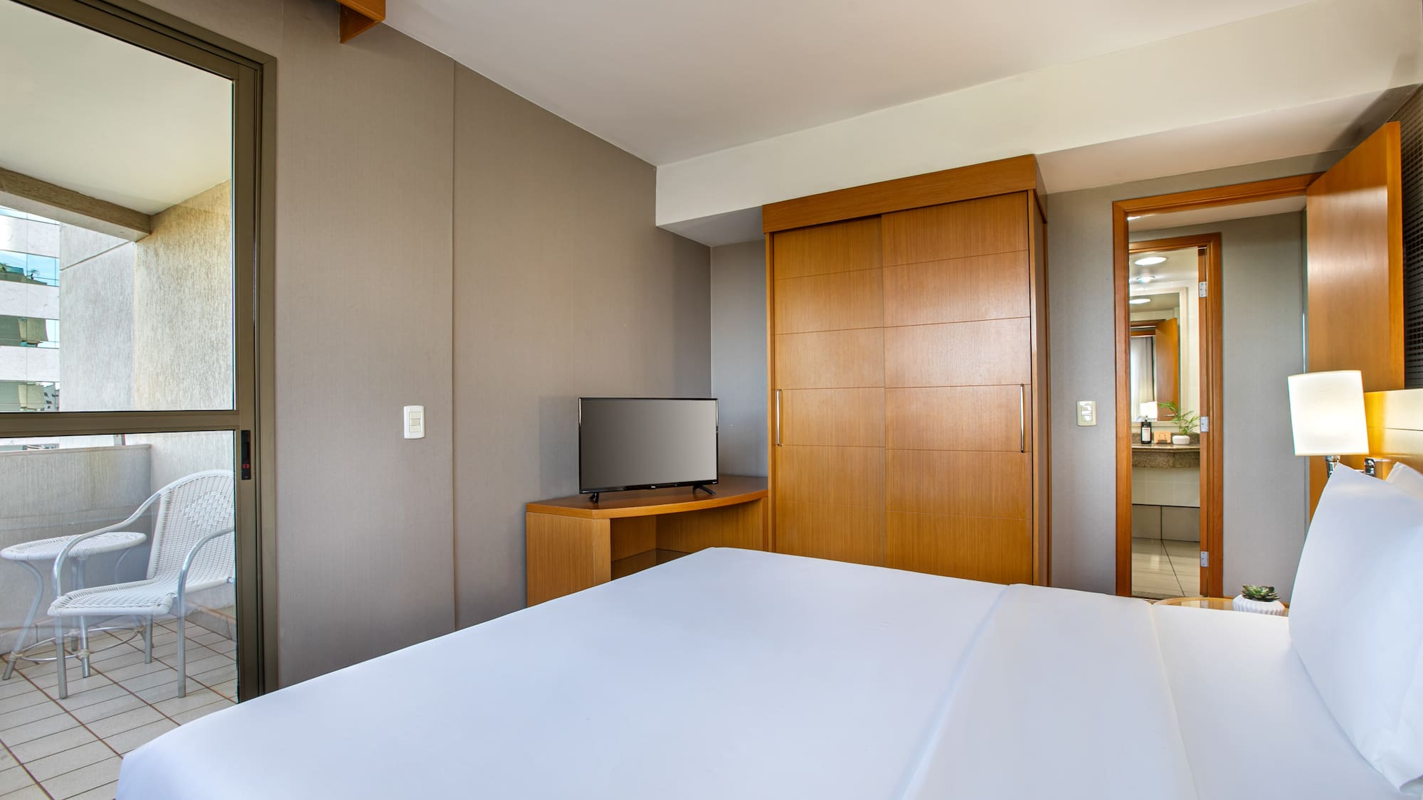 Clean hotel room with large white bed, TV, wooden wardrobe, and balcony.