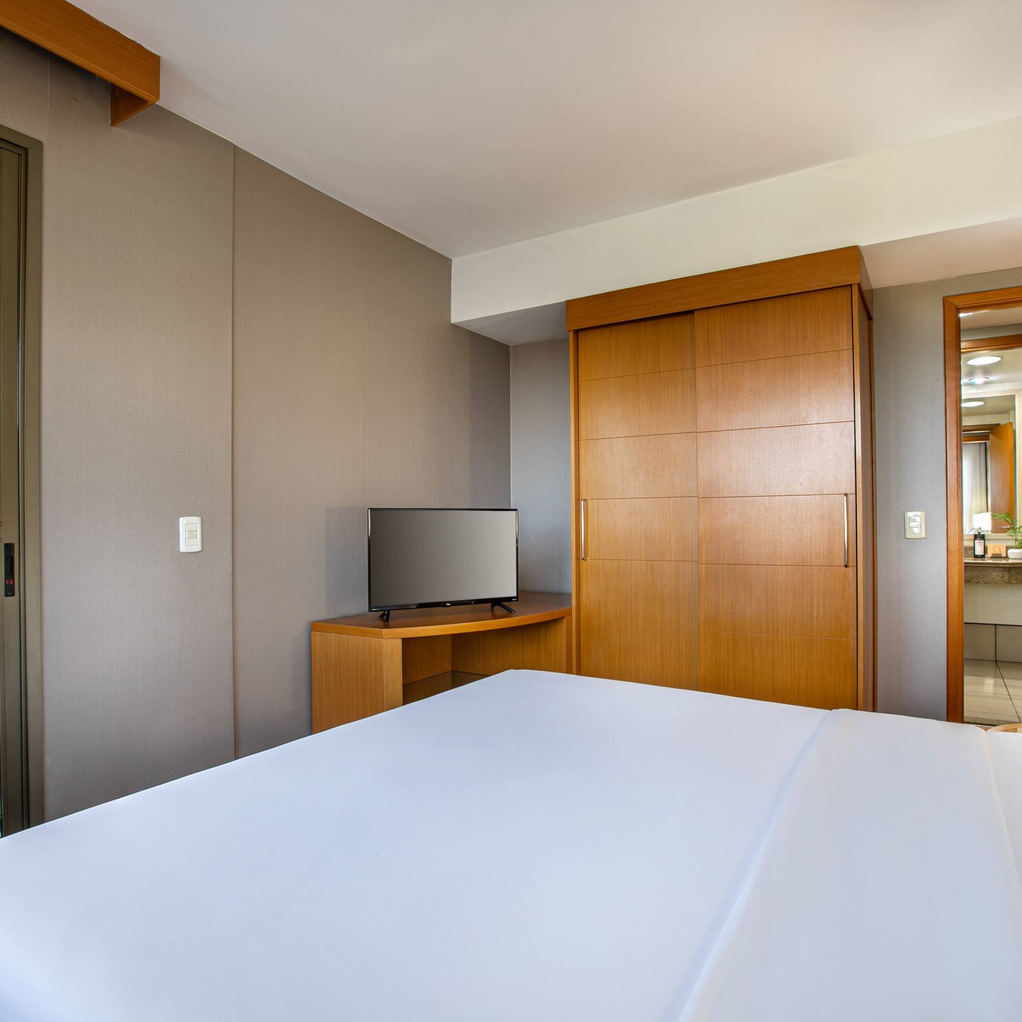 Clean hotel room with large white bed, TV, wooden wardrobe, and balcony.