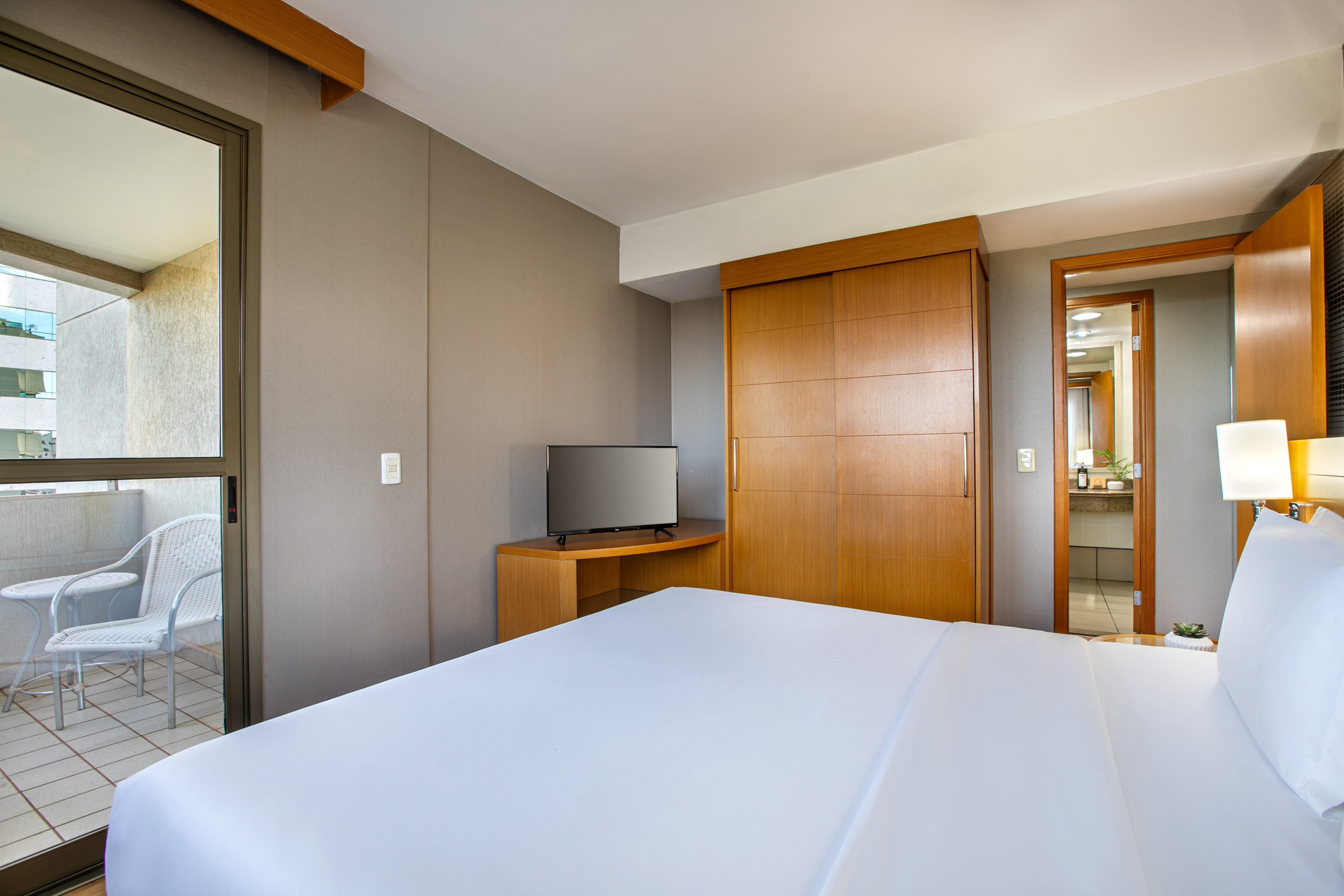 Clean hotel room with large white bed, TV, wooden wardrobe, and balcony.