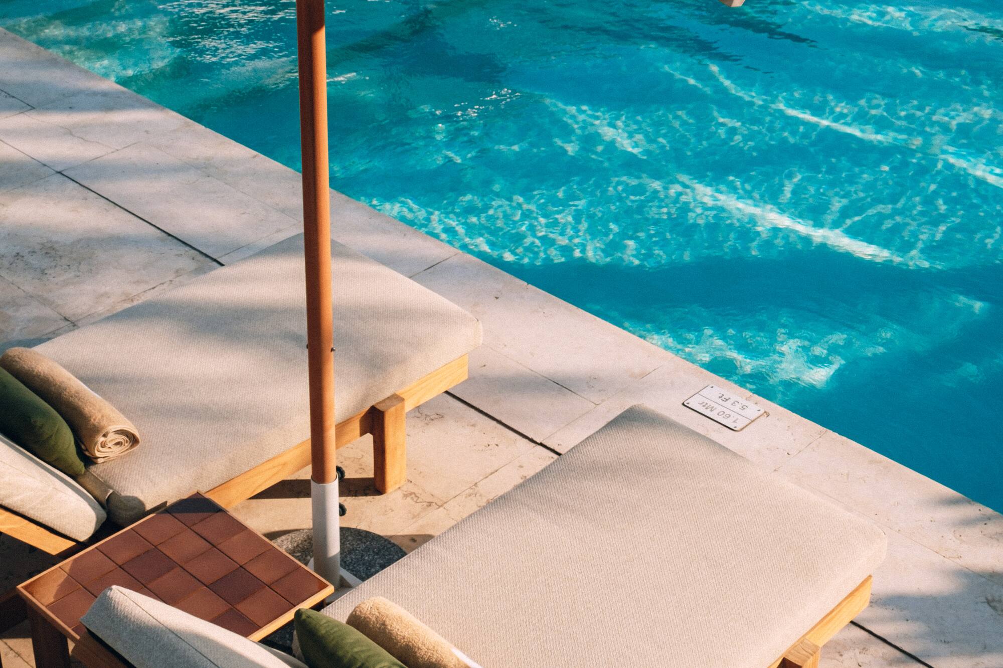 Resort poolside: two lounge chairs, white umbrella, and shimmering blue water.