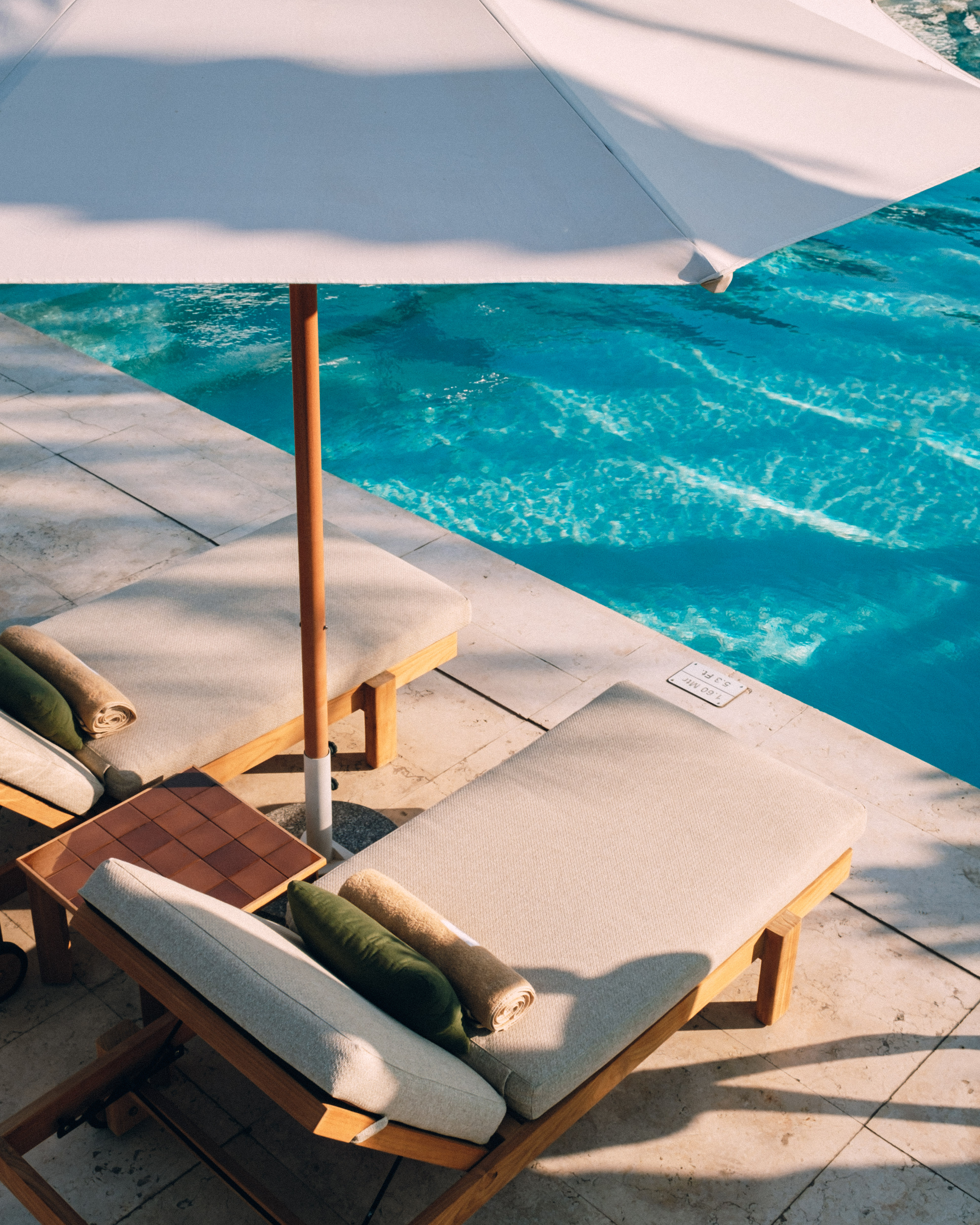 Resort poolside: two lounge chairs, white umbrella, and shimmering blue water.