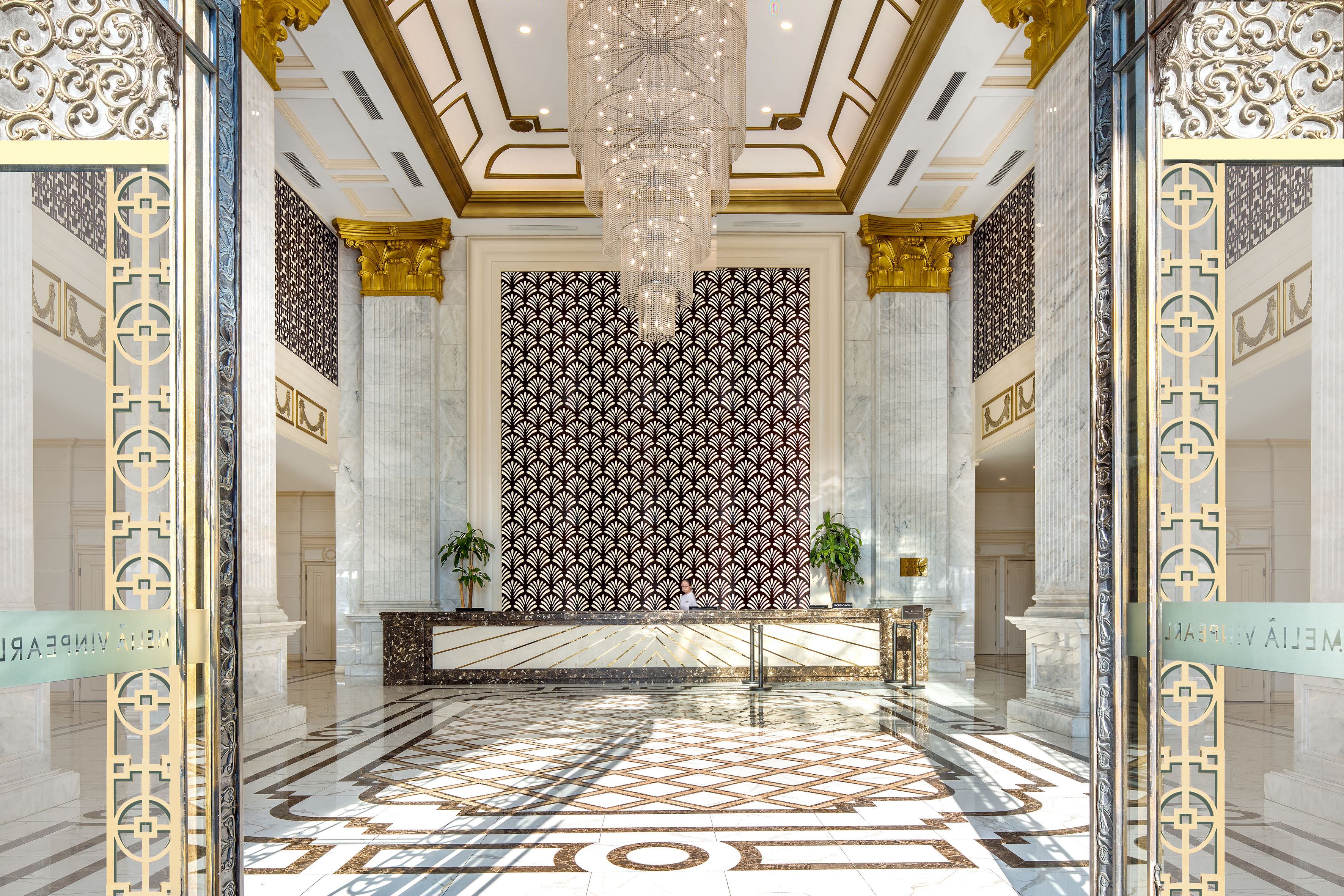 Luxurious hotel lobby with crystal chandelier, marble, gold decor, reception.