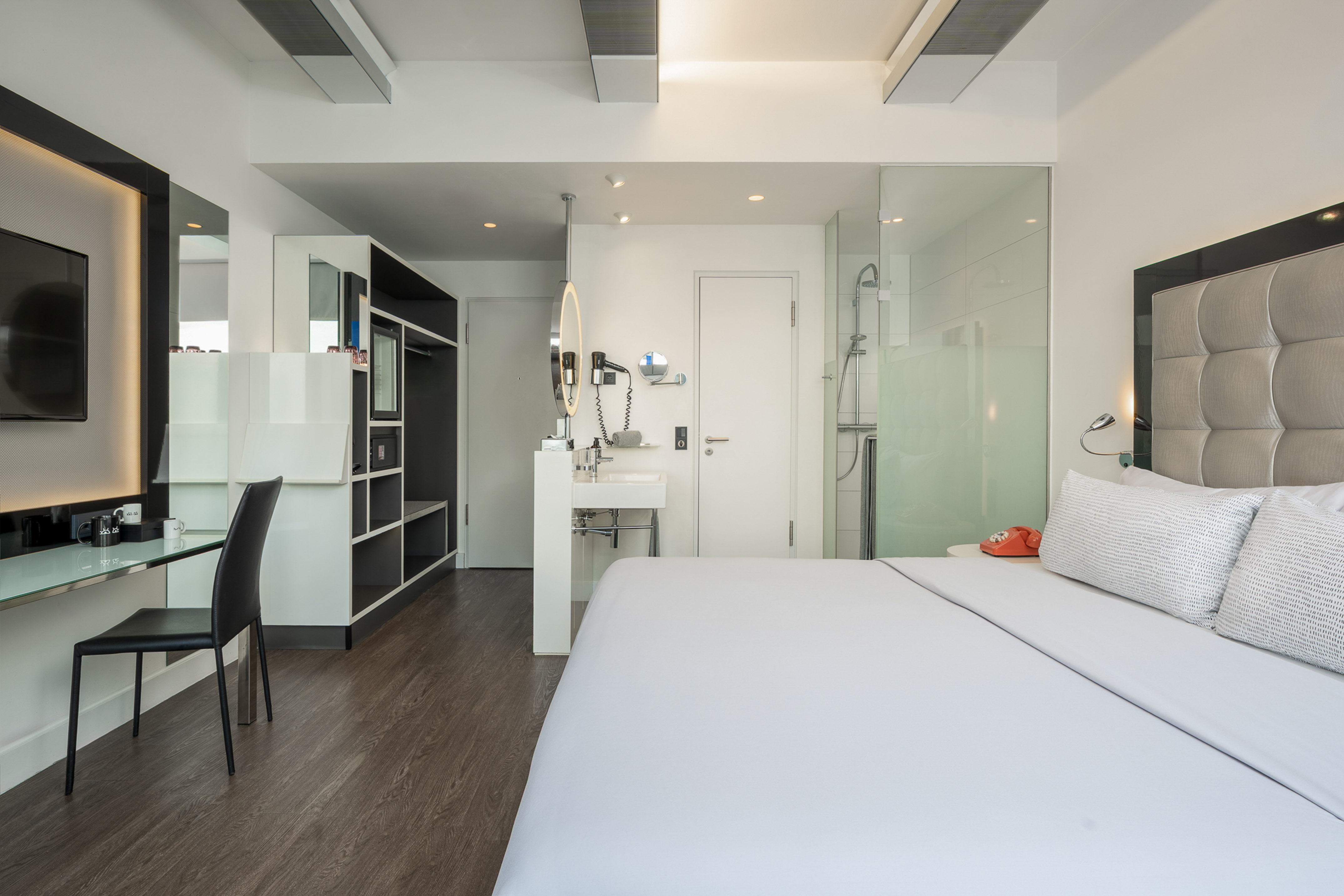 Modern hotel room with bed, integrated workspace, and glass shower.