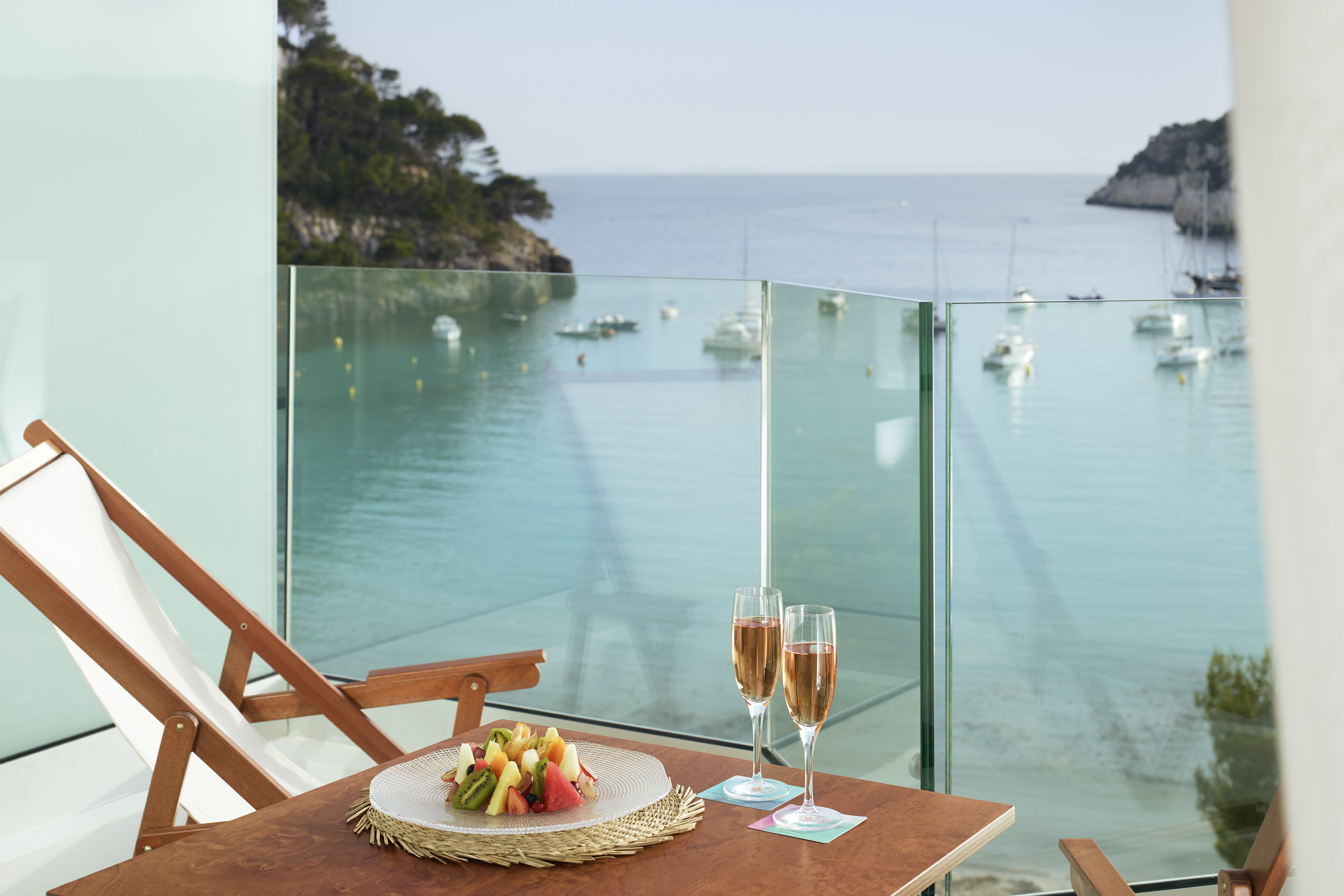 Hotel balcony with fruit, champagne, and beautiful Mediterranean bay view.