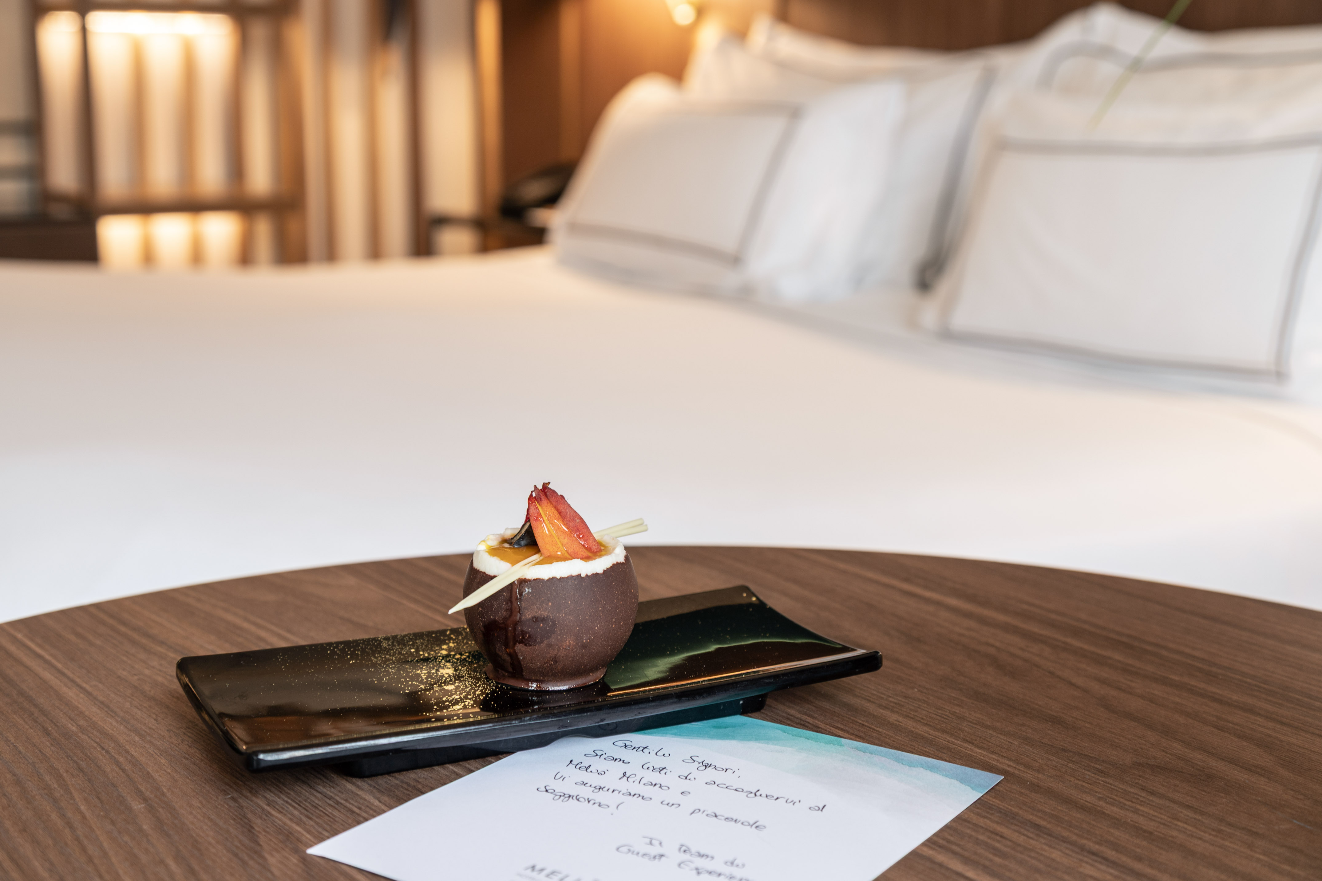 Hotel welcome amenity: chocolate dessert with fruit garnish, guest note, hotel room.