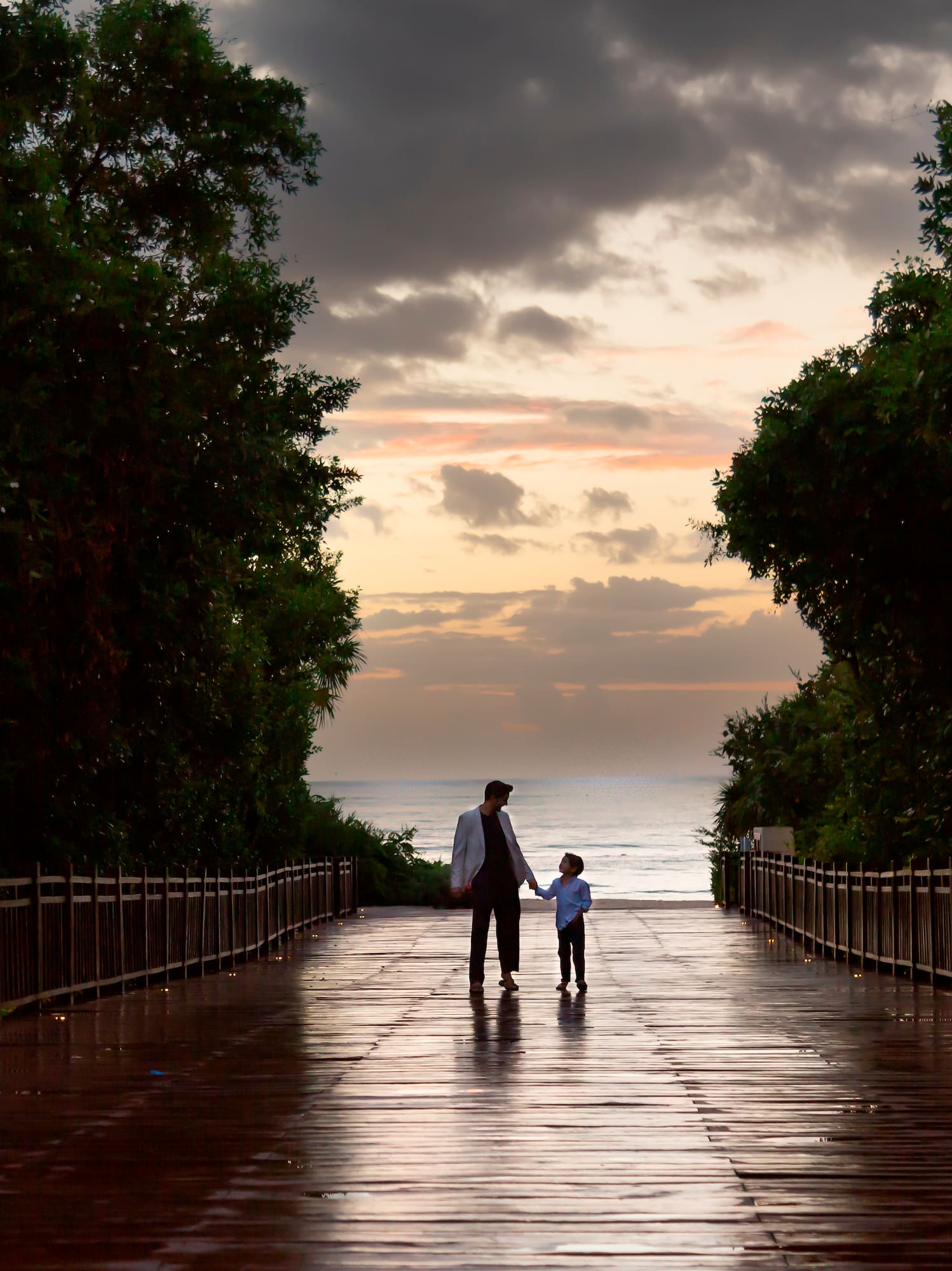 a man and child walking on a wet walkway with trees and water