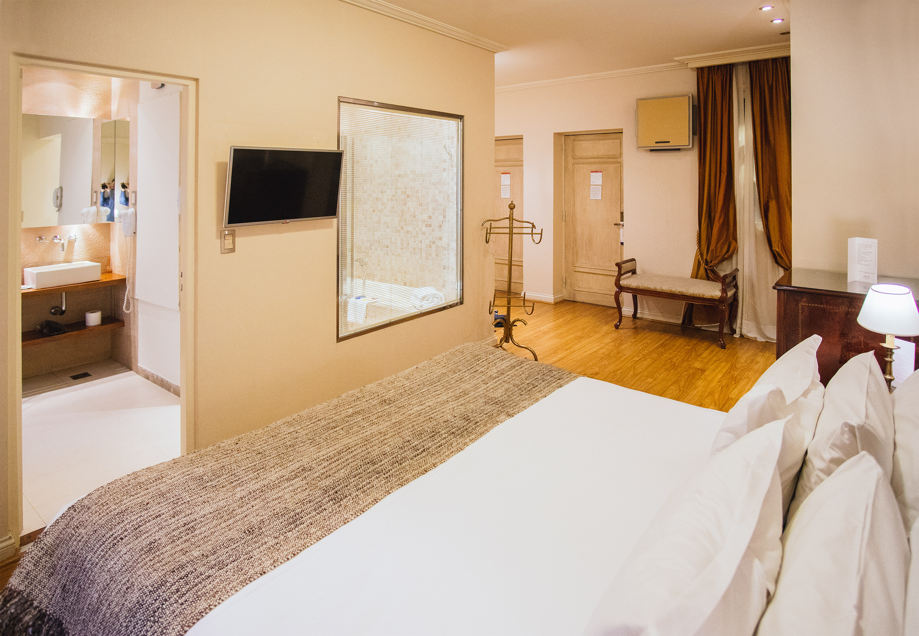 Modern hotel bedroom with white bed, wall-mounted TV, and bright bathroom.
