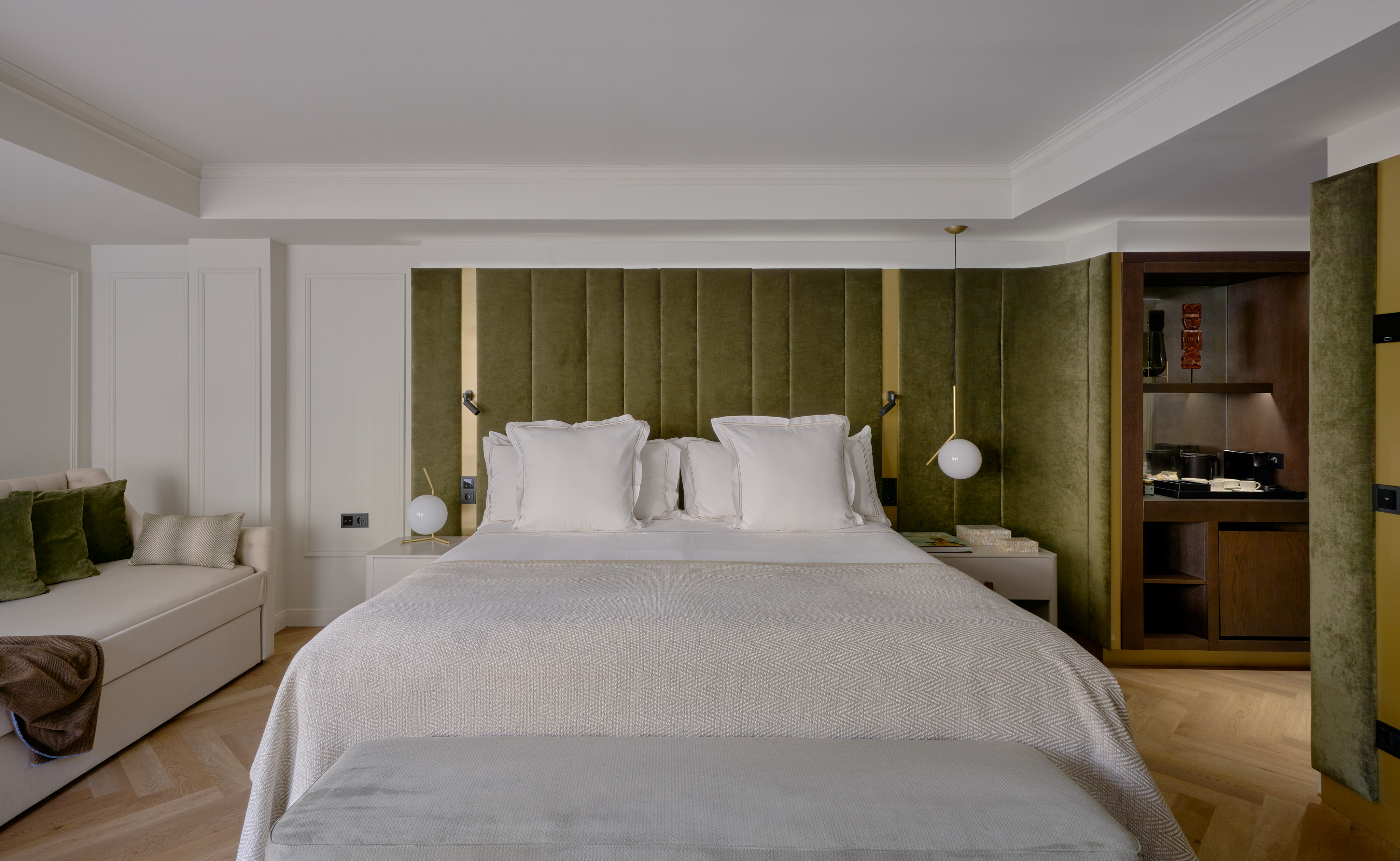Modern luxury bedroom with green velvet headboard, white bed, and herringbone floor.
