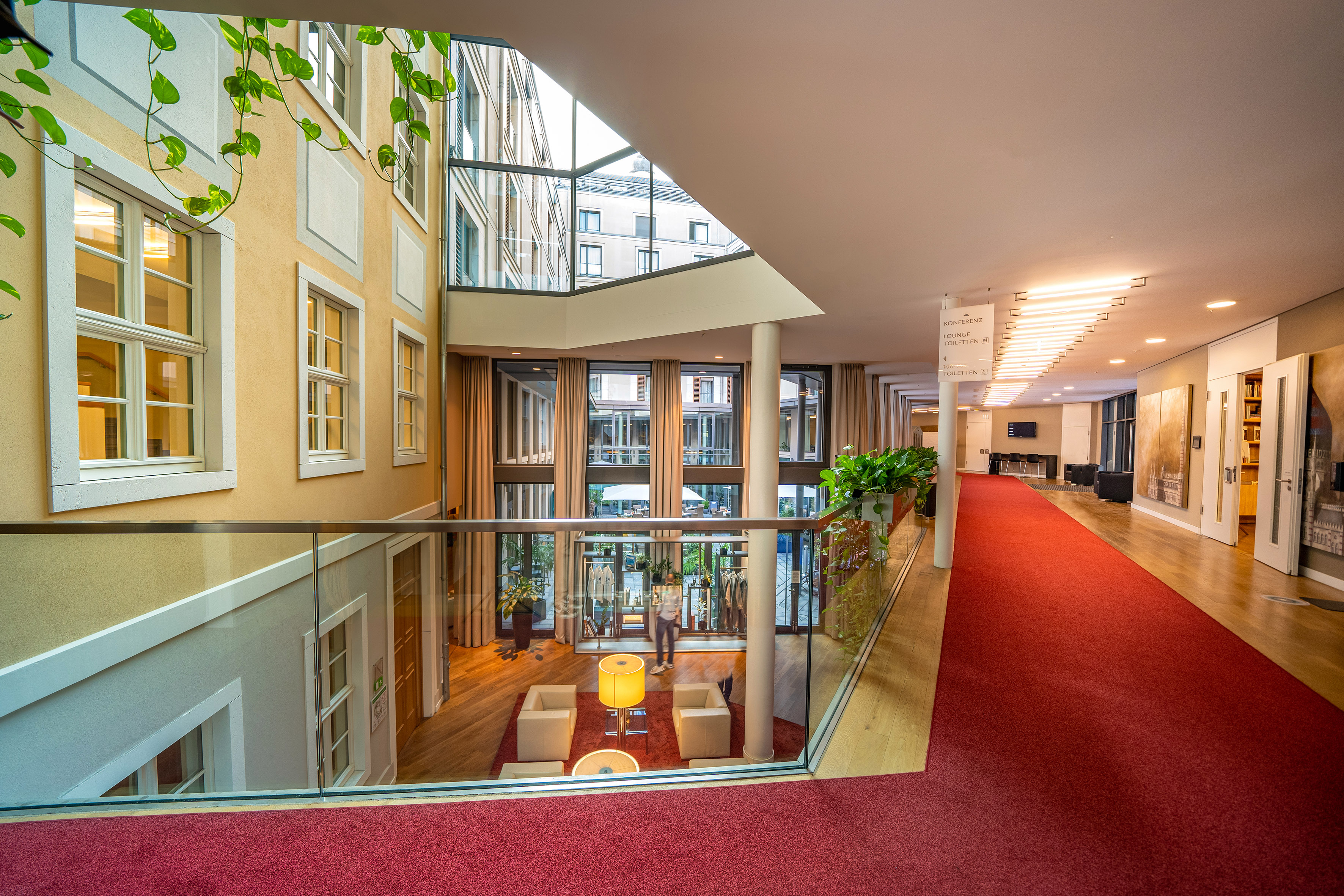 Multi-level hotel lobby with red carpet, glass atrium, and lounge area.