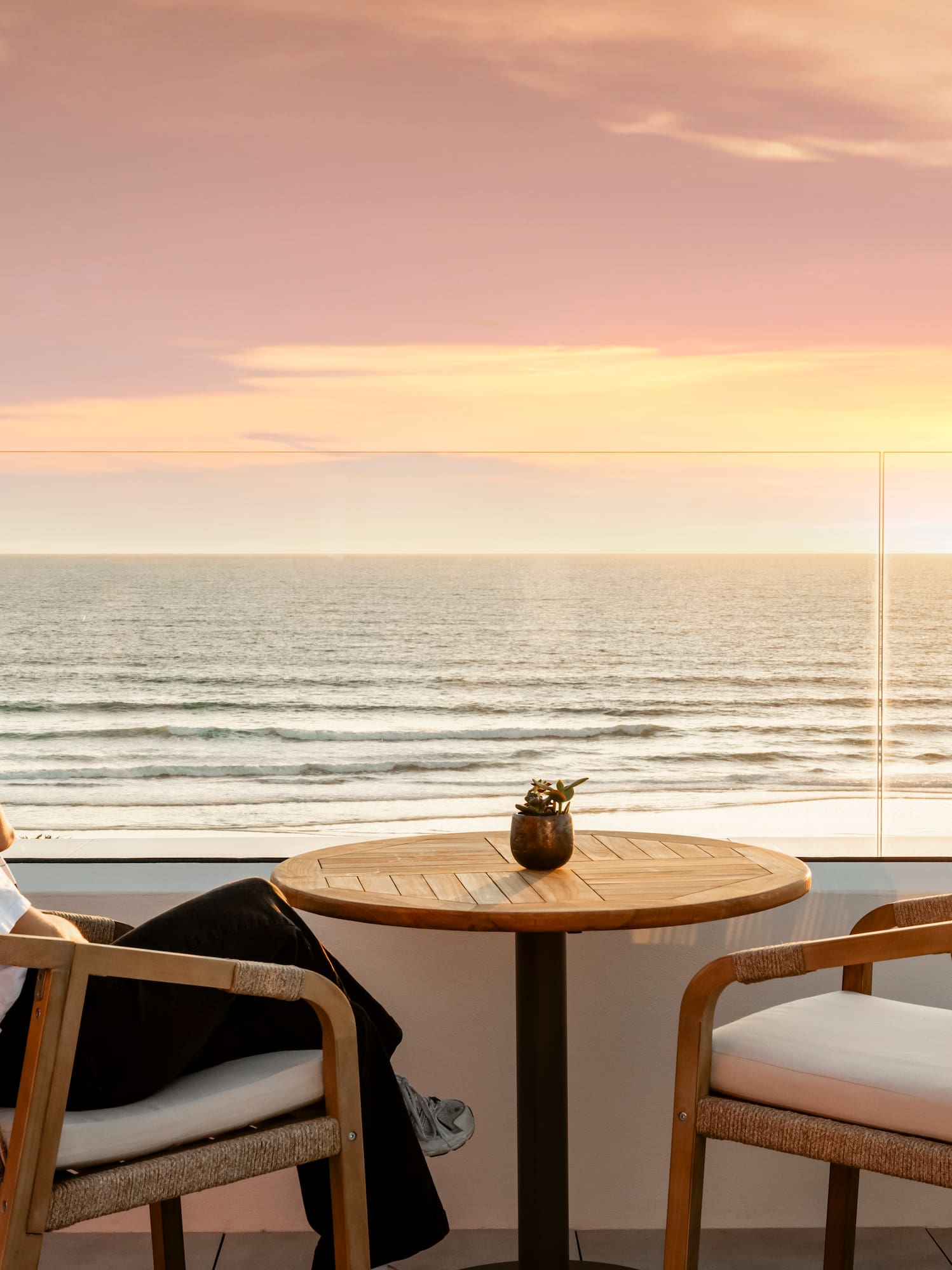Mujer relajándose en terraza con atardecer sobre el océano.