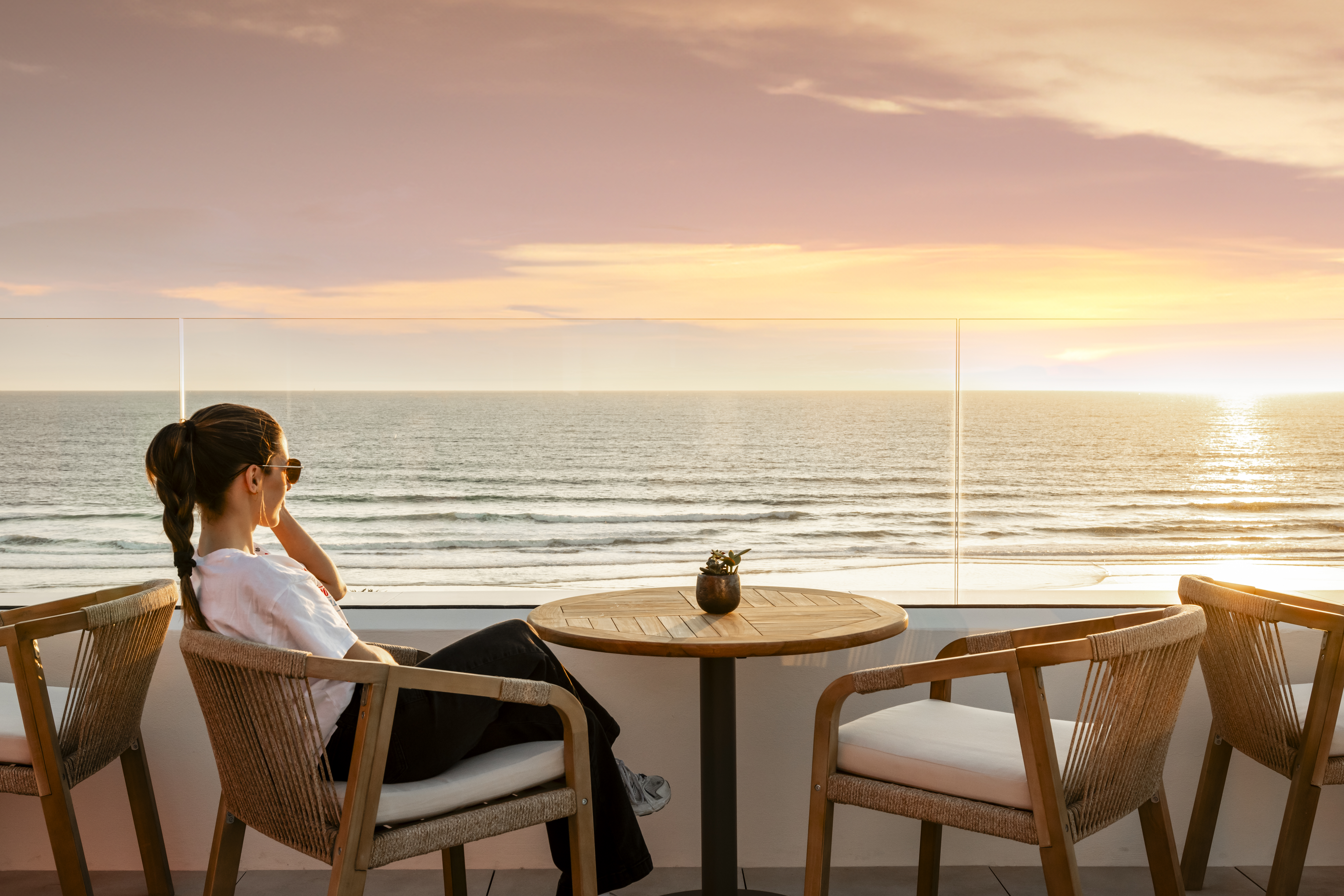 Mujer relajándose en terraza con atardecer sobre el océano.