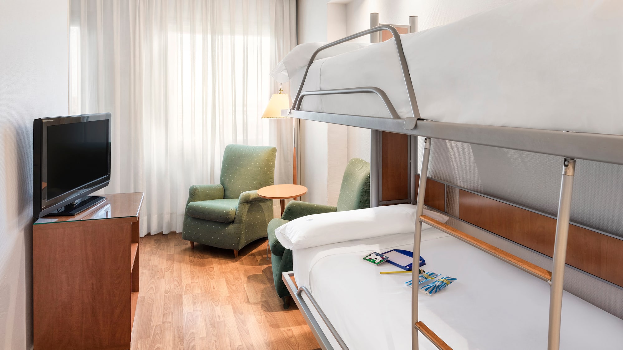 Hotel family room with metal bunk beds, television, and green armchairs.