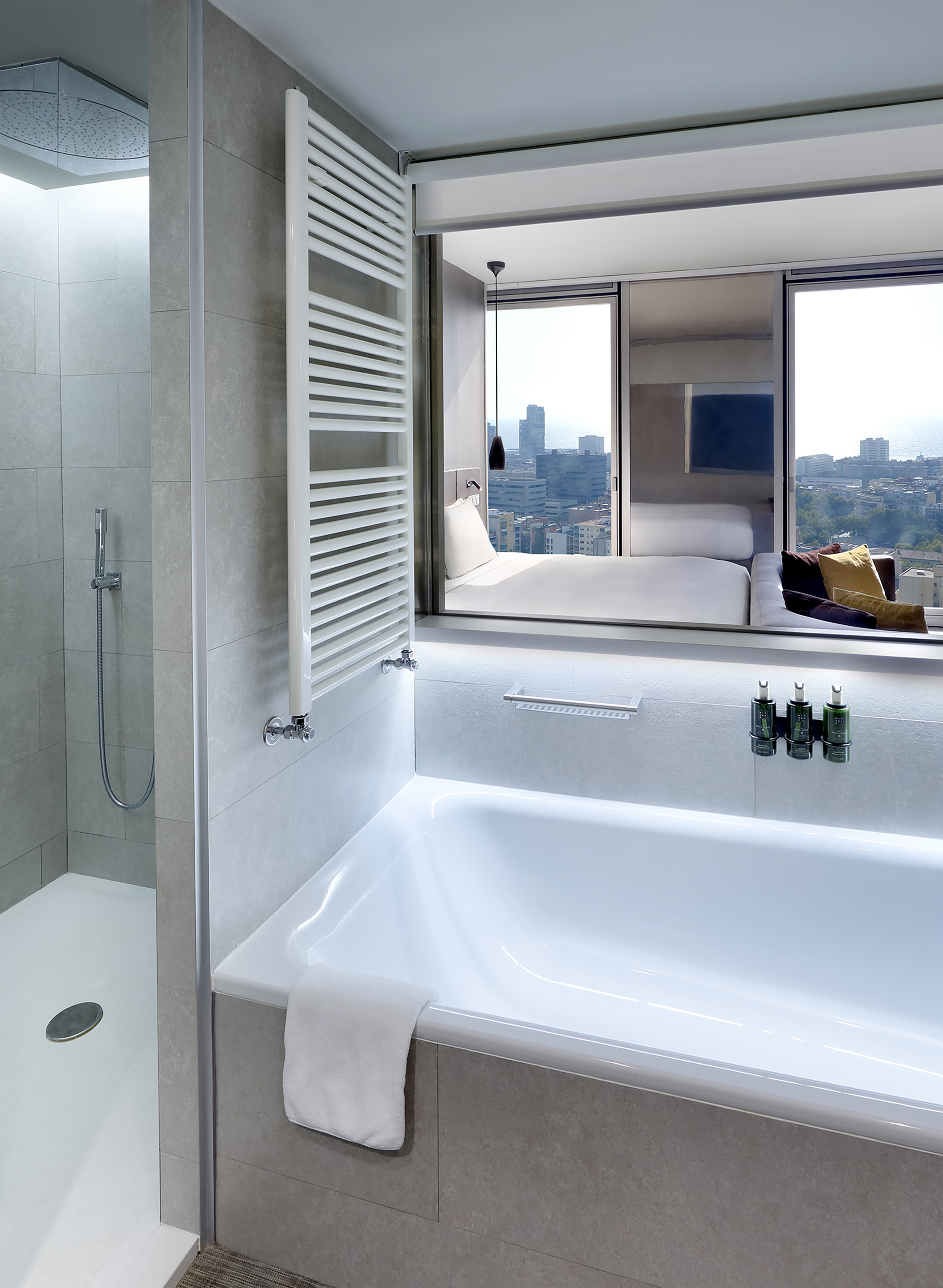 Modern hotel bathroom with bathtub, shower, towel warmer, and city view.