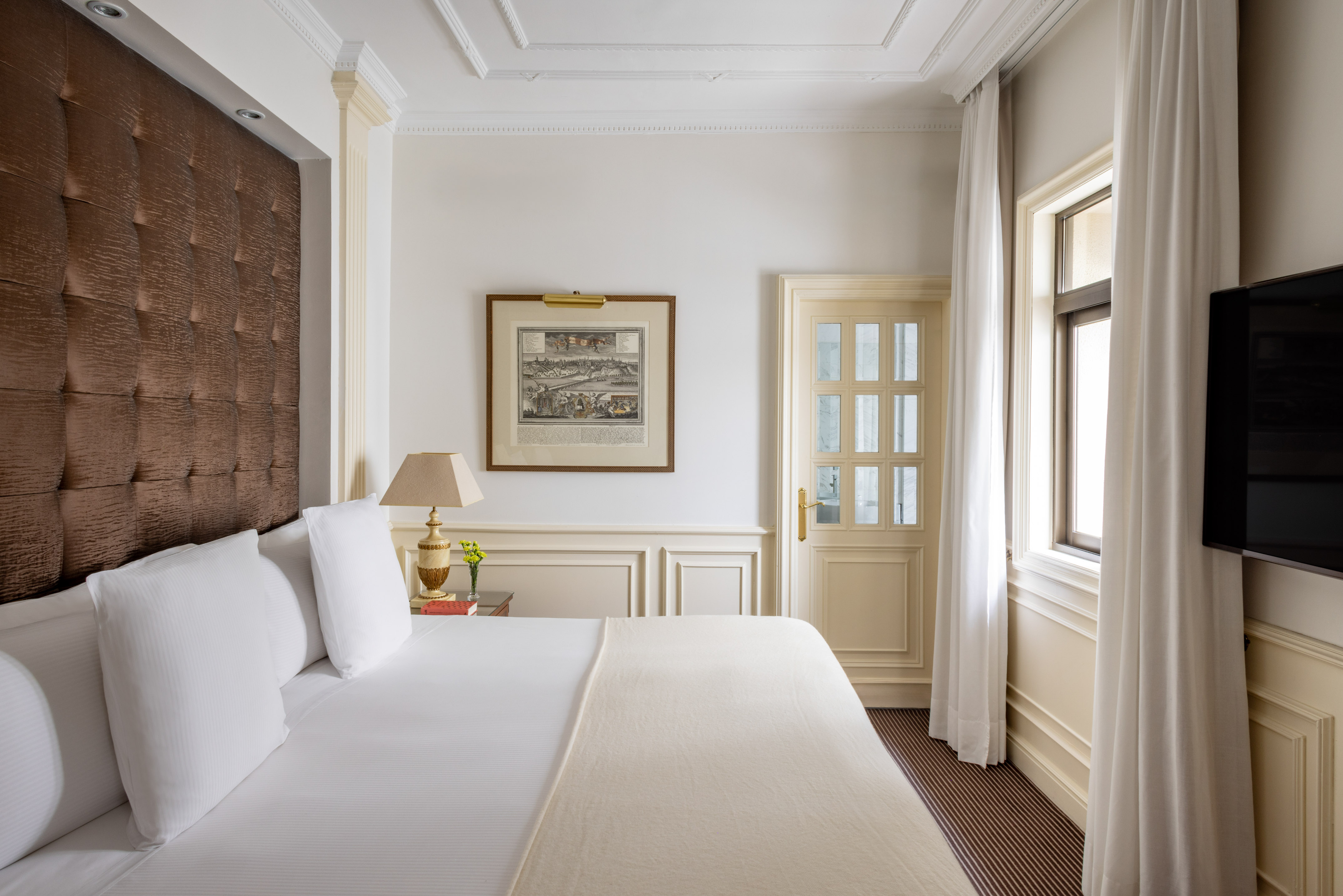 Elegant hotel bedroom: white bed, brown tufted headboard, map art, classic decor.