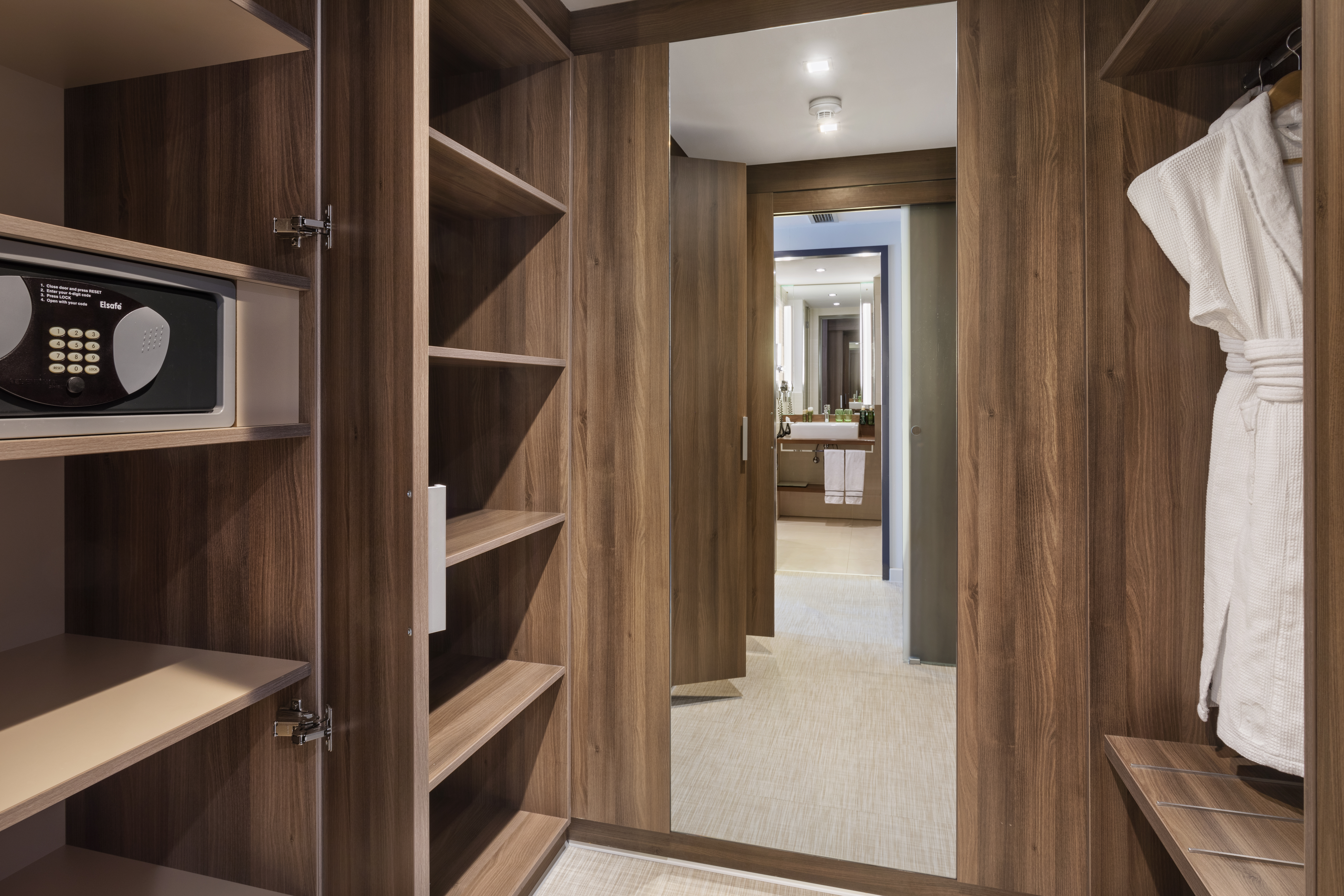 Hotel room closet with security safe, shelves, robe, and bathroom entrance.