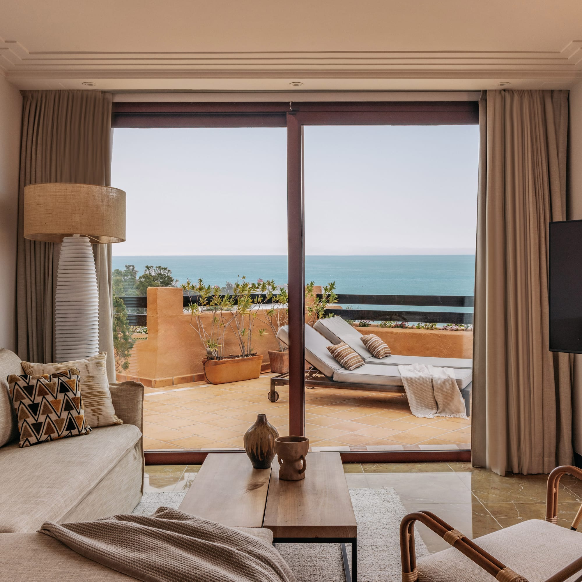 Coastal living room with ocean view balcony, sofa, and outdoor lounge chairs.