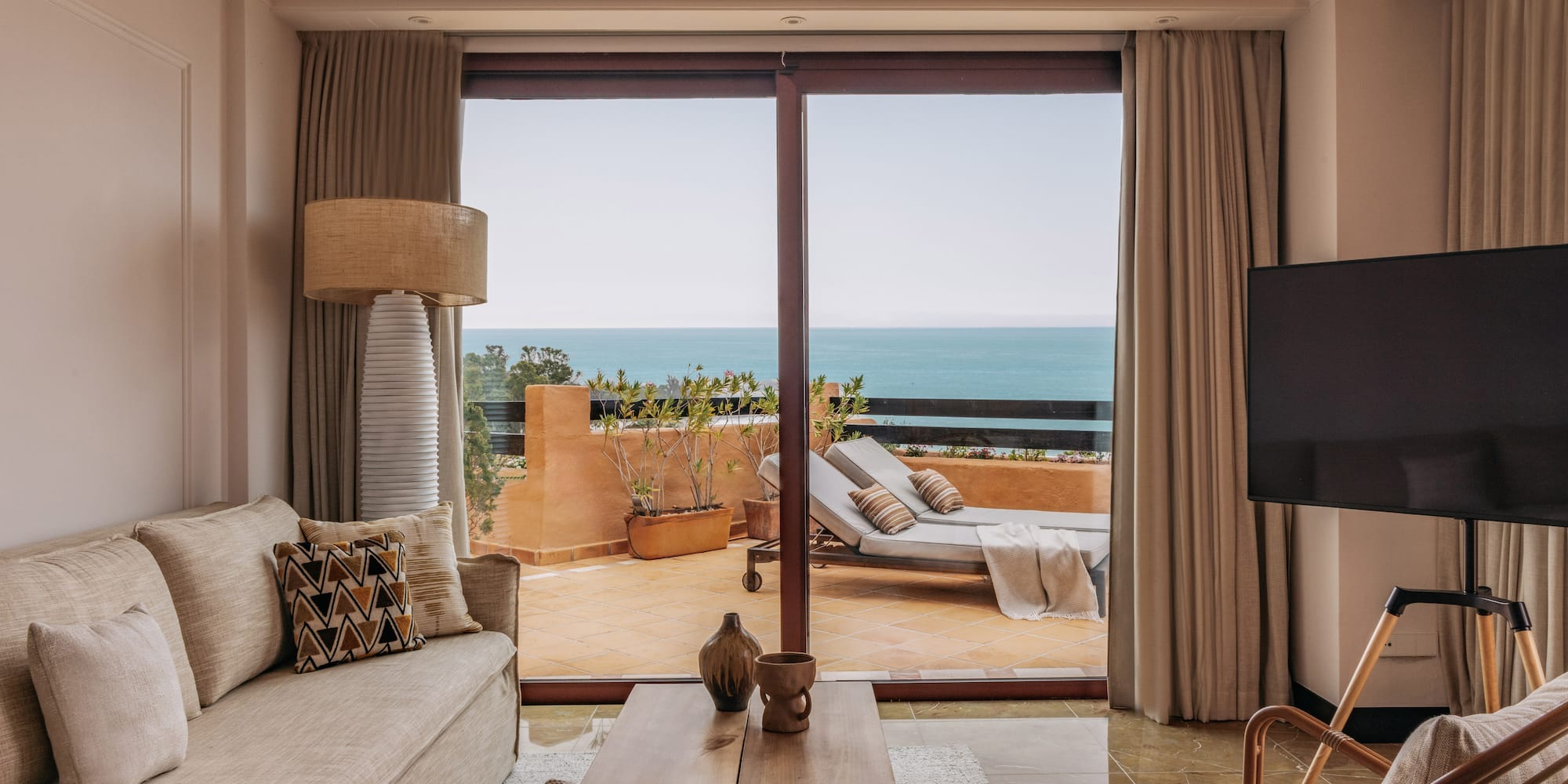 Coastal living room with ocean view balcony, sofa, and outdoor lounge chairs.