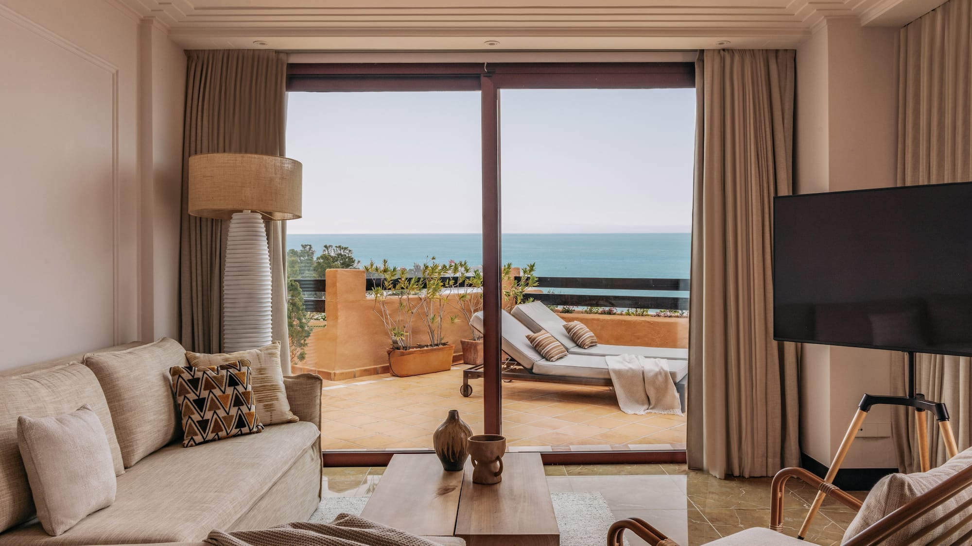 Coastal living room with ocean view balcony, sofa, and outdoor lounge chairs.