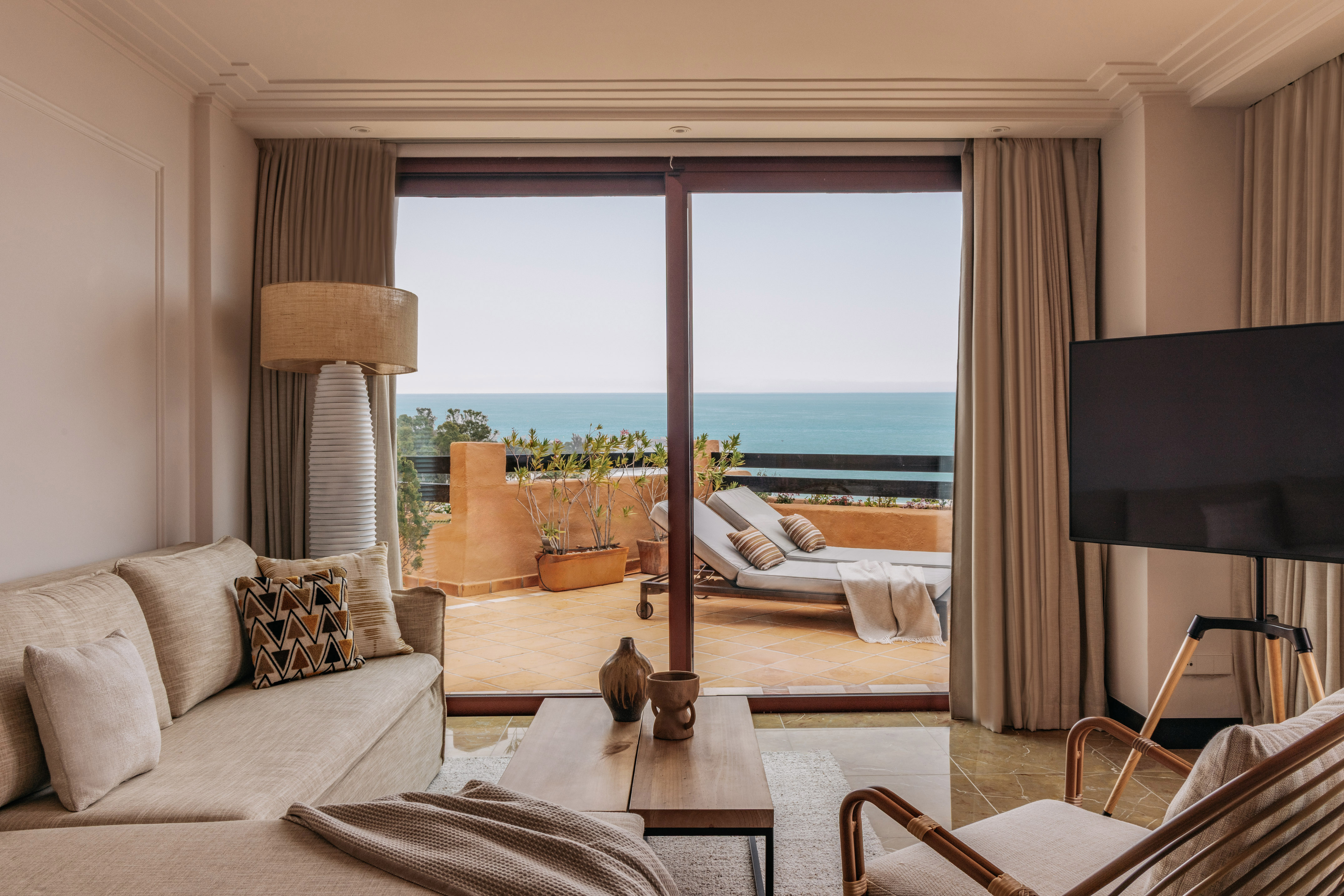 Coastal living room with ocean view balcony, sofa, and outdoor lounge chairs.