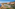 Coastal resort with orange hotels, sports courts, swimming pools, ocean, and mountains.