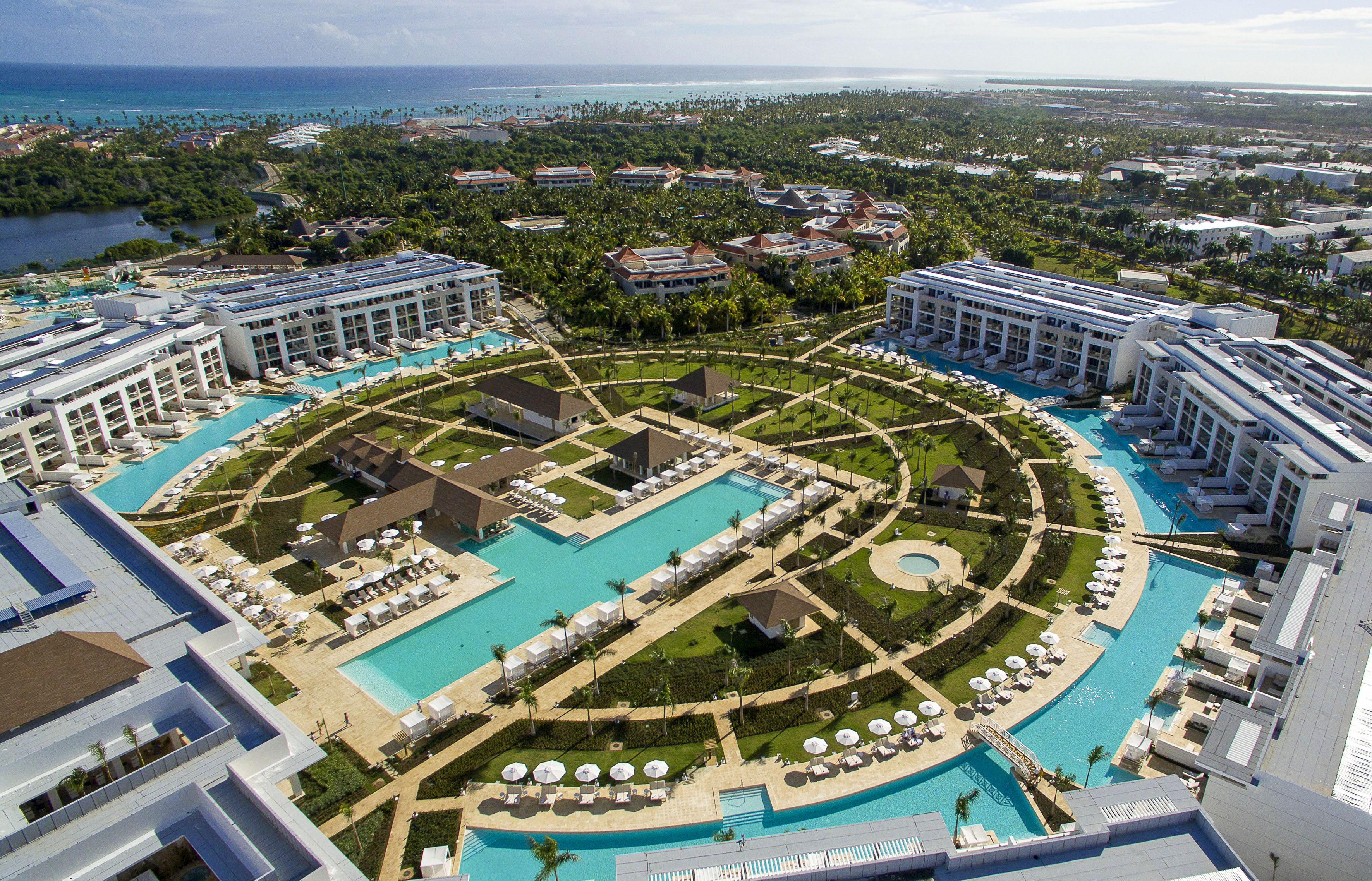Aerial luxury resort, vast turquoise pools, modern buildings, lush landscaping, oceanfront.