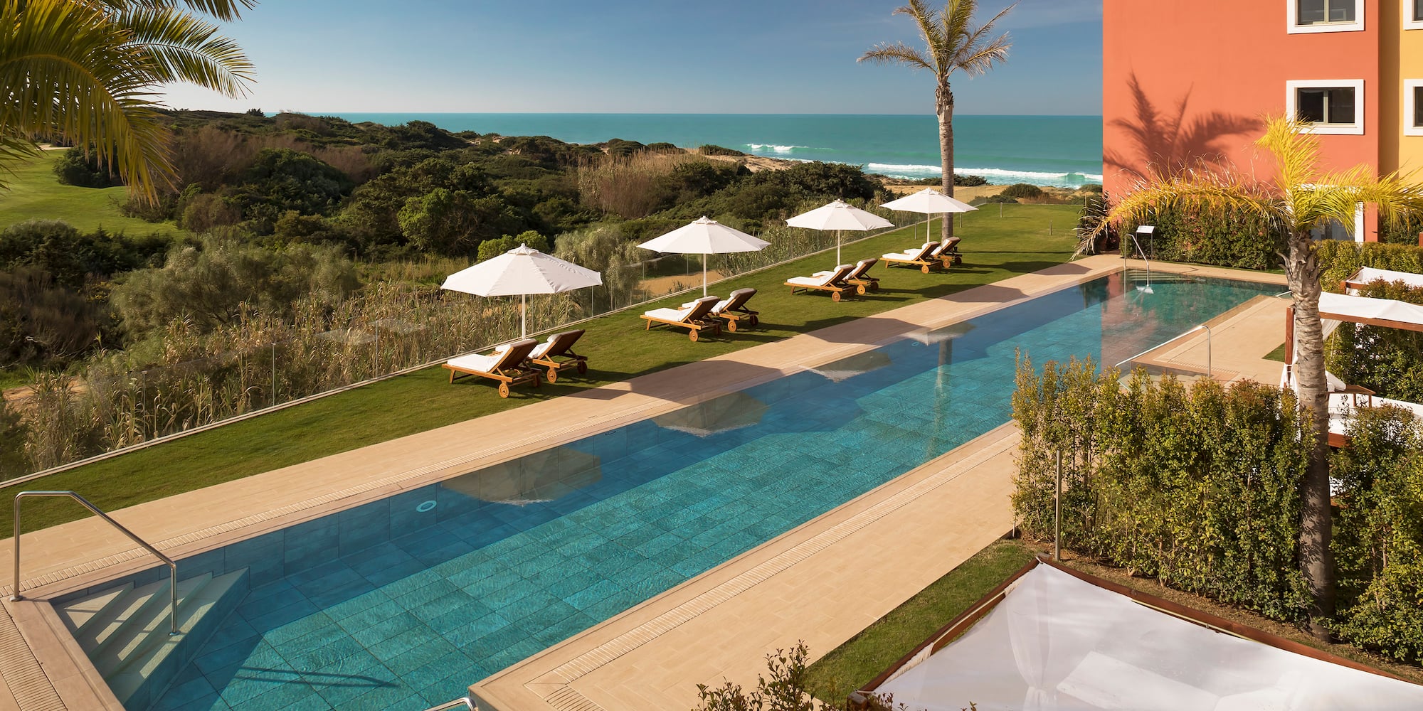 a pool with lounge chairs and umbrellas by a building