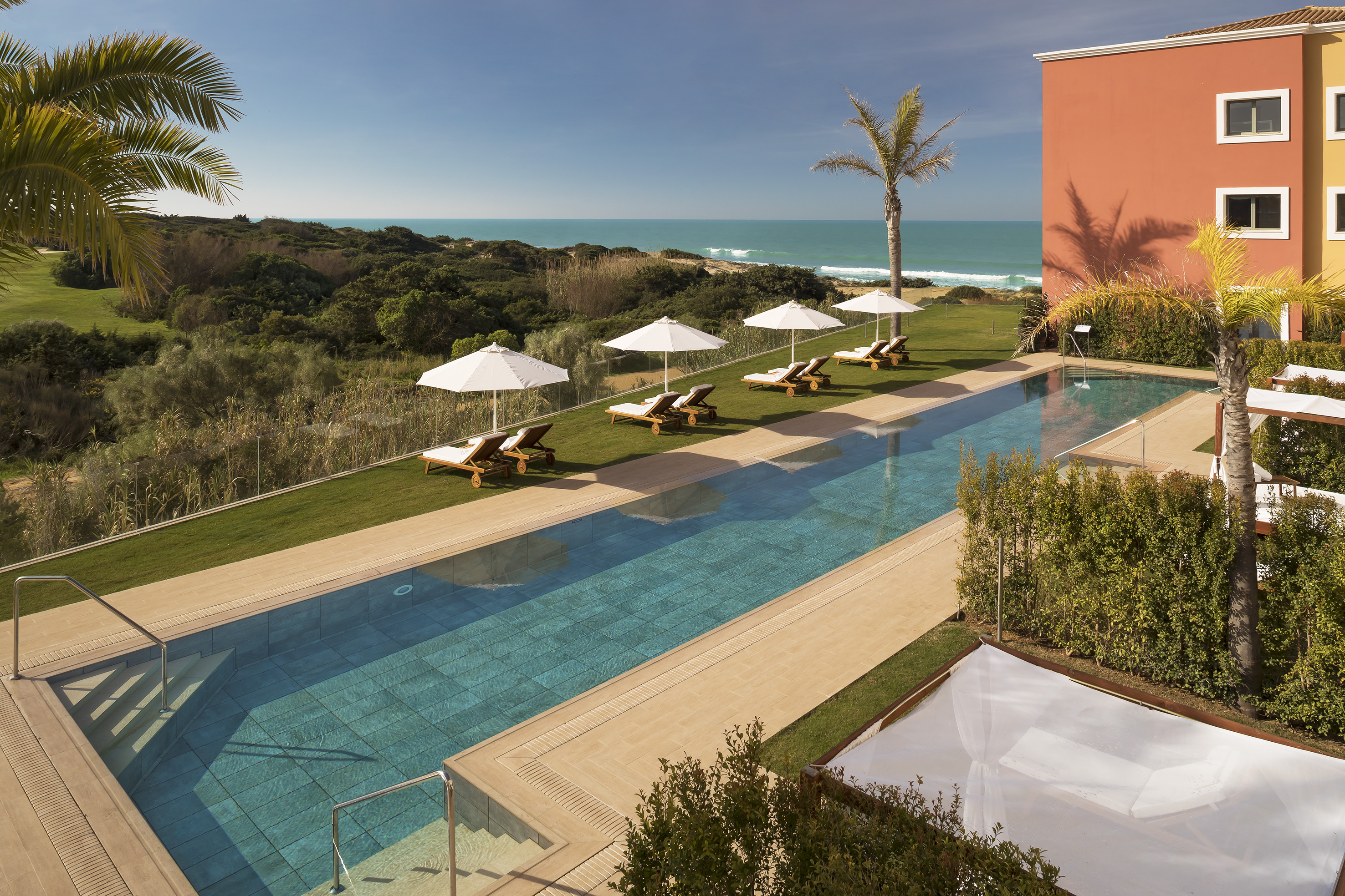 a pool with lounge chairs and umbrellas by a building