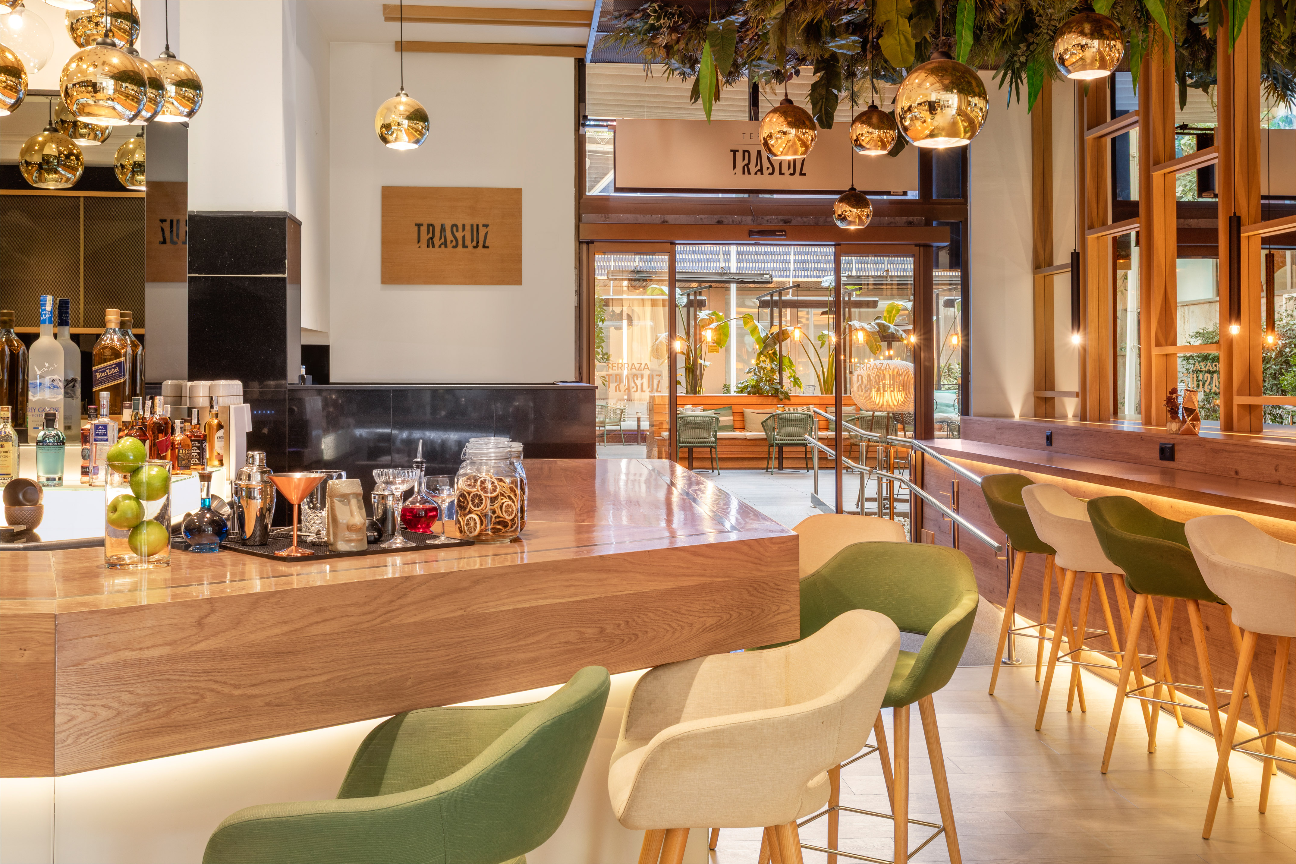 Trasluz bar with wooden counter, cocktail setup, green stools, golden lights.