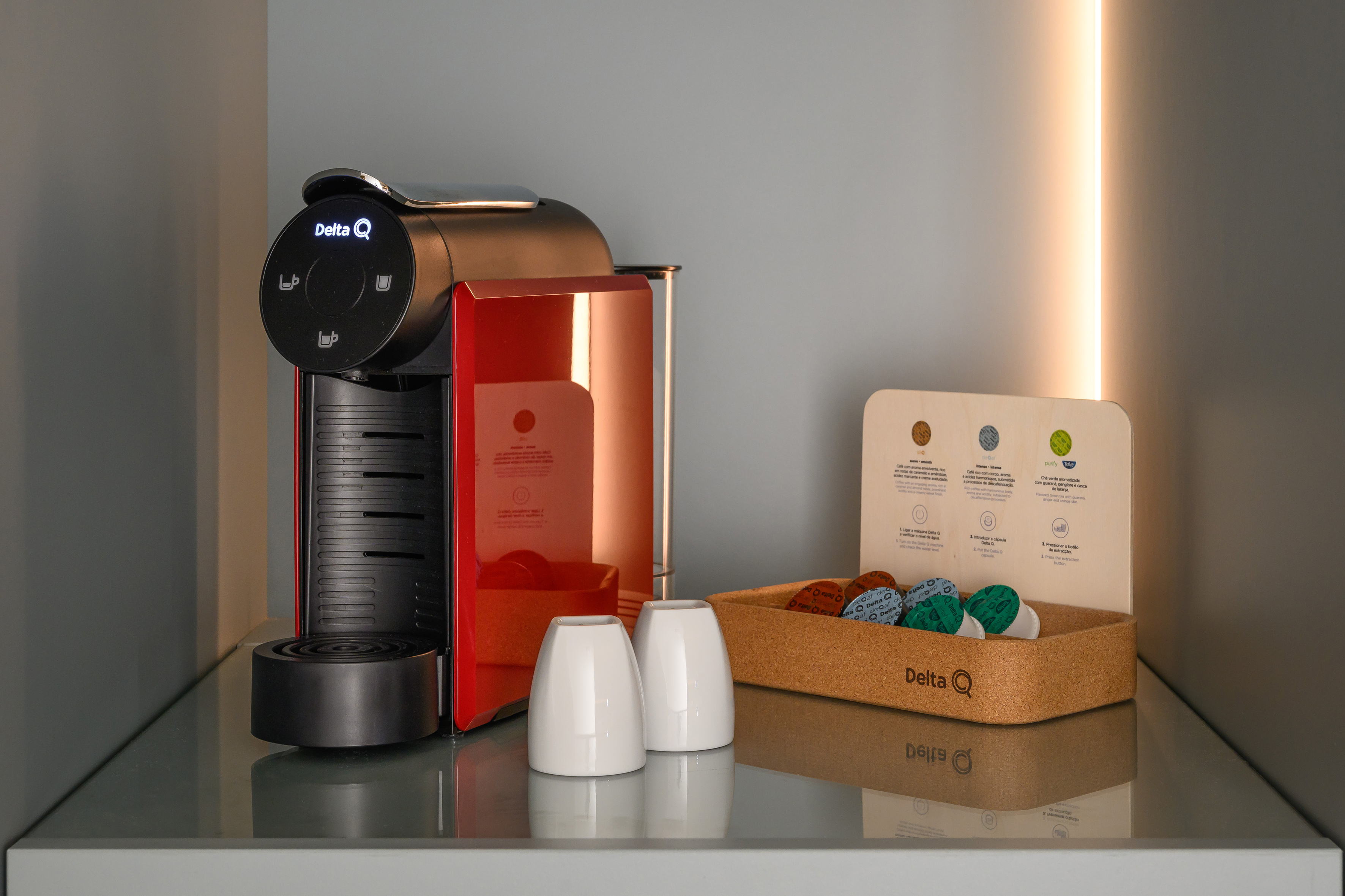Red Delta Q coffee maker, capsules, and two white cups with display.